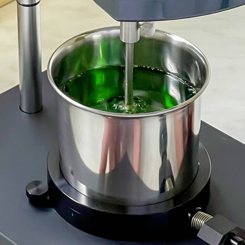 Een metalen pot met groene vloeistof wordt geroerd door een roertoestel.