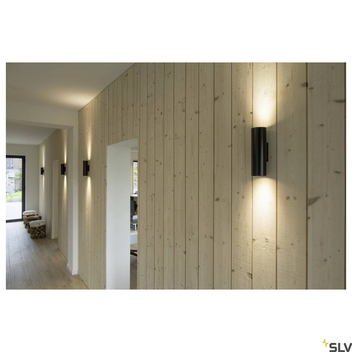 Een houten hal met moderne zwarte wandlampen die warm licht werpen op de beschoten wand, naast een open doorgang.