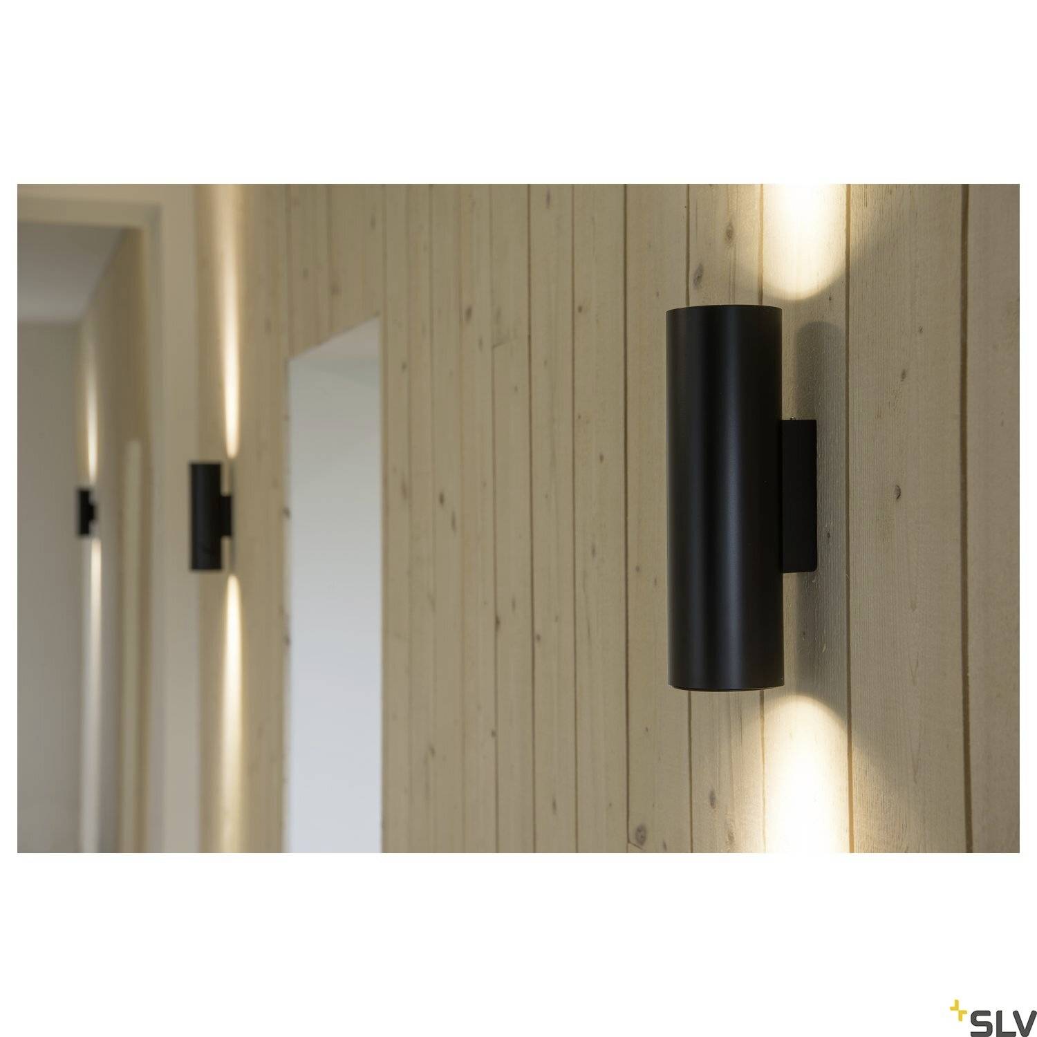 Zwarte wandlampen aan een lichte houten lambrisering creëren een warm, gericht lichtpatroon naar boven en beneden langs de wand.