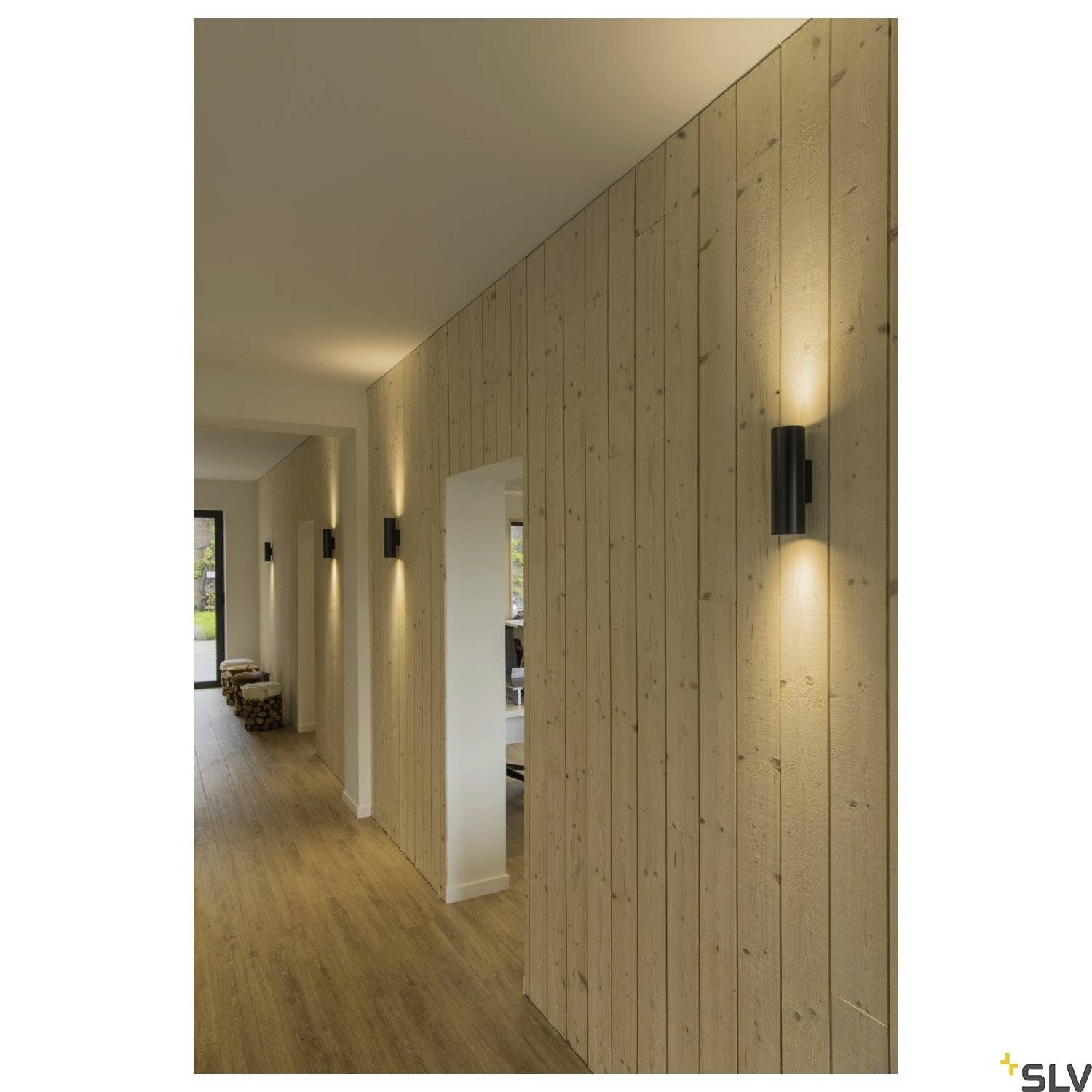Gang met houten wandbekleding en moderne wandlampen die een warm licht verspreiden. Houten vloer en meerdere zitgelegenheden aan het einde.