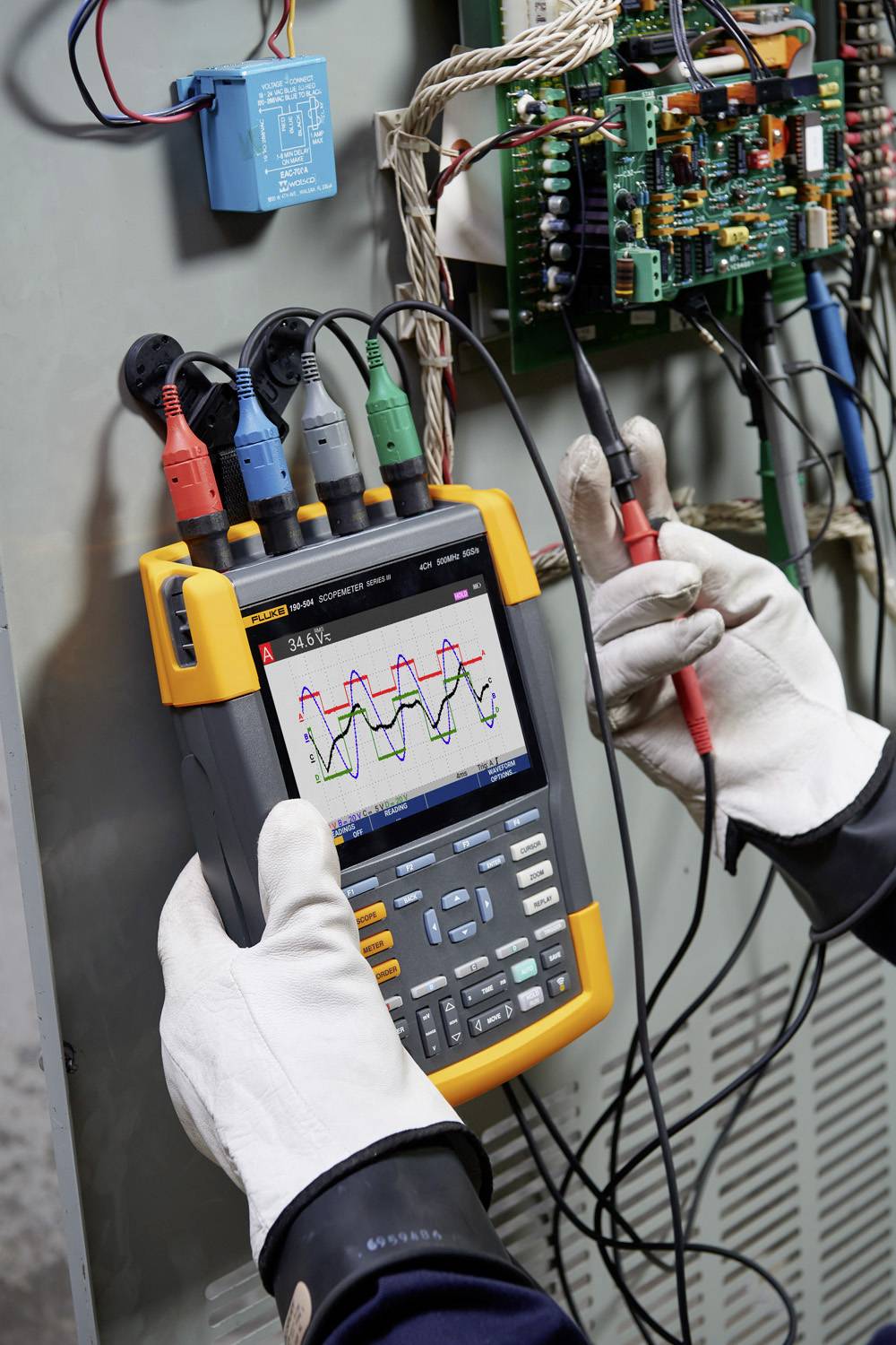 Een technicus gebruikt een digitale oscilloscoop met gekleurde sondes om elektrische signalen te meten aan een schakelkast.