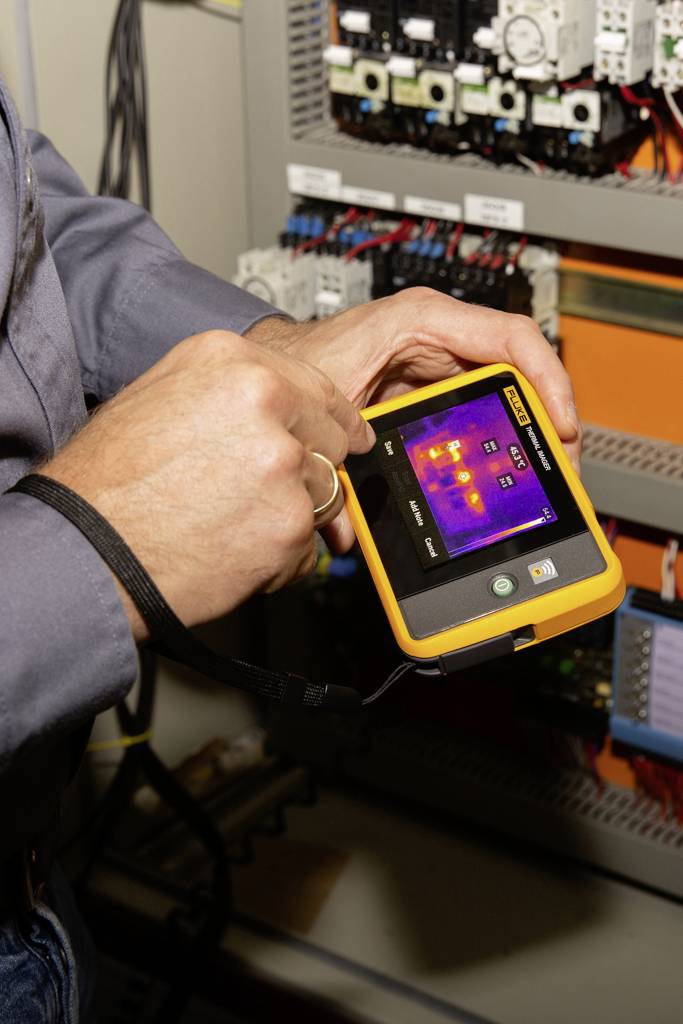 Een persoon houdt een meetinstrument vast dat een warmtebeeld van een elektrische schakelkast weergeeft.