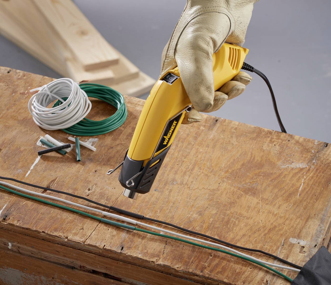 Een gele elektrische kabelkniptang, vastgehouden door een gehandschoende hand, knipt kabels op een houten tafel. Ernaast liggen extra kabels.