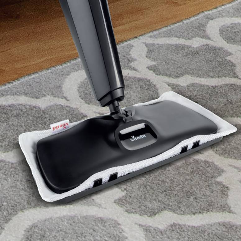 Een dweil met een zwarte steel glijdt over een vloerkleed dat gedeeltelijk over een houten vloer is gelegd.