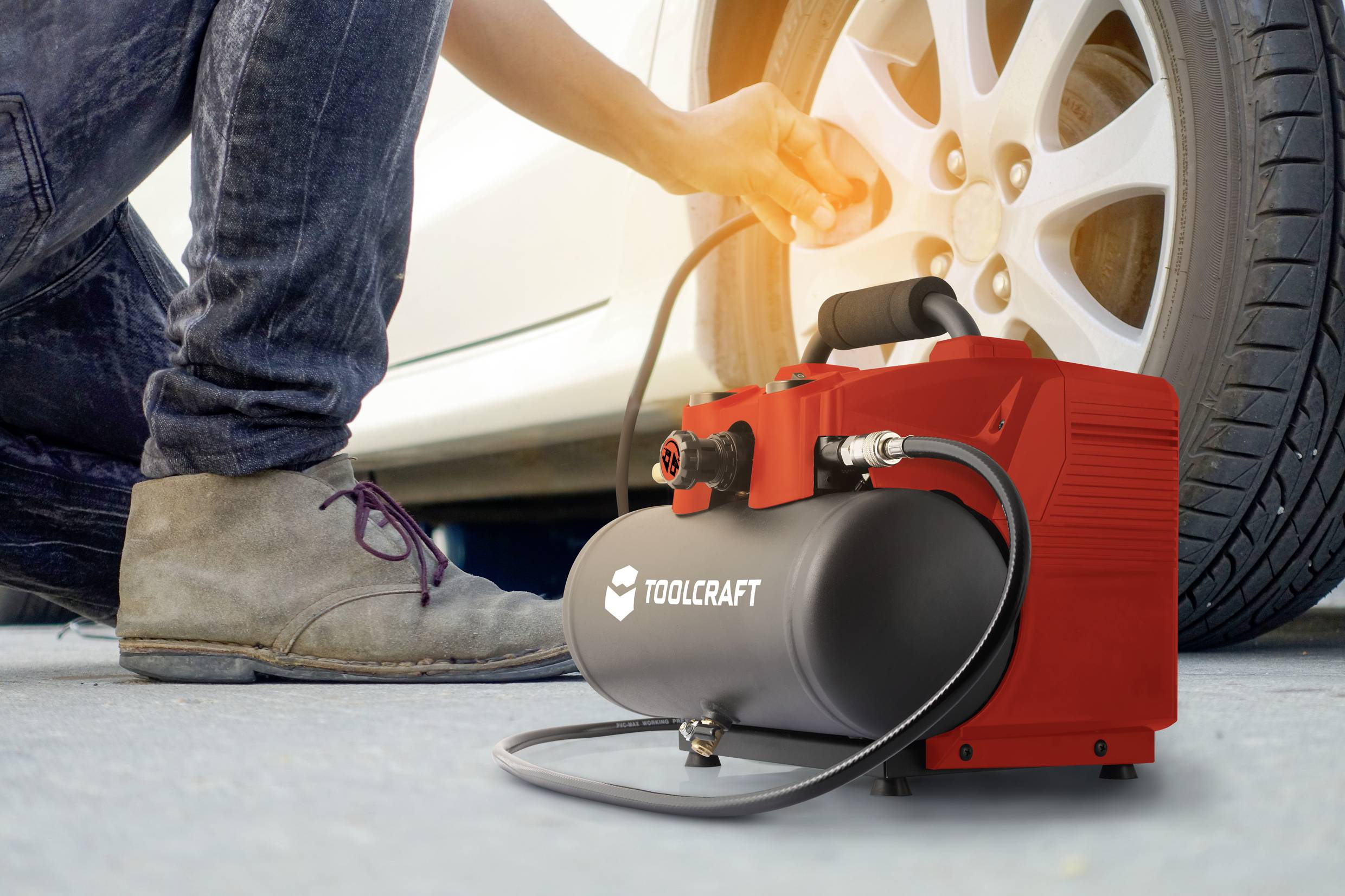 Een persoon controleert de bandenspanning van een witte auto met een kleine rode compressor. De compressor is verbonden met de auto.