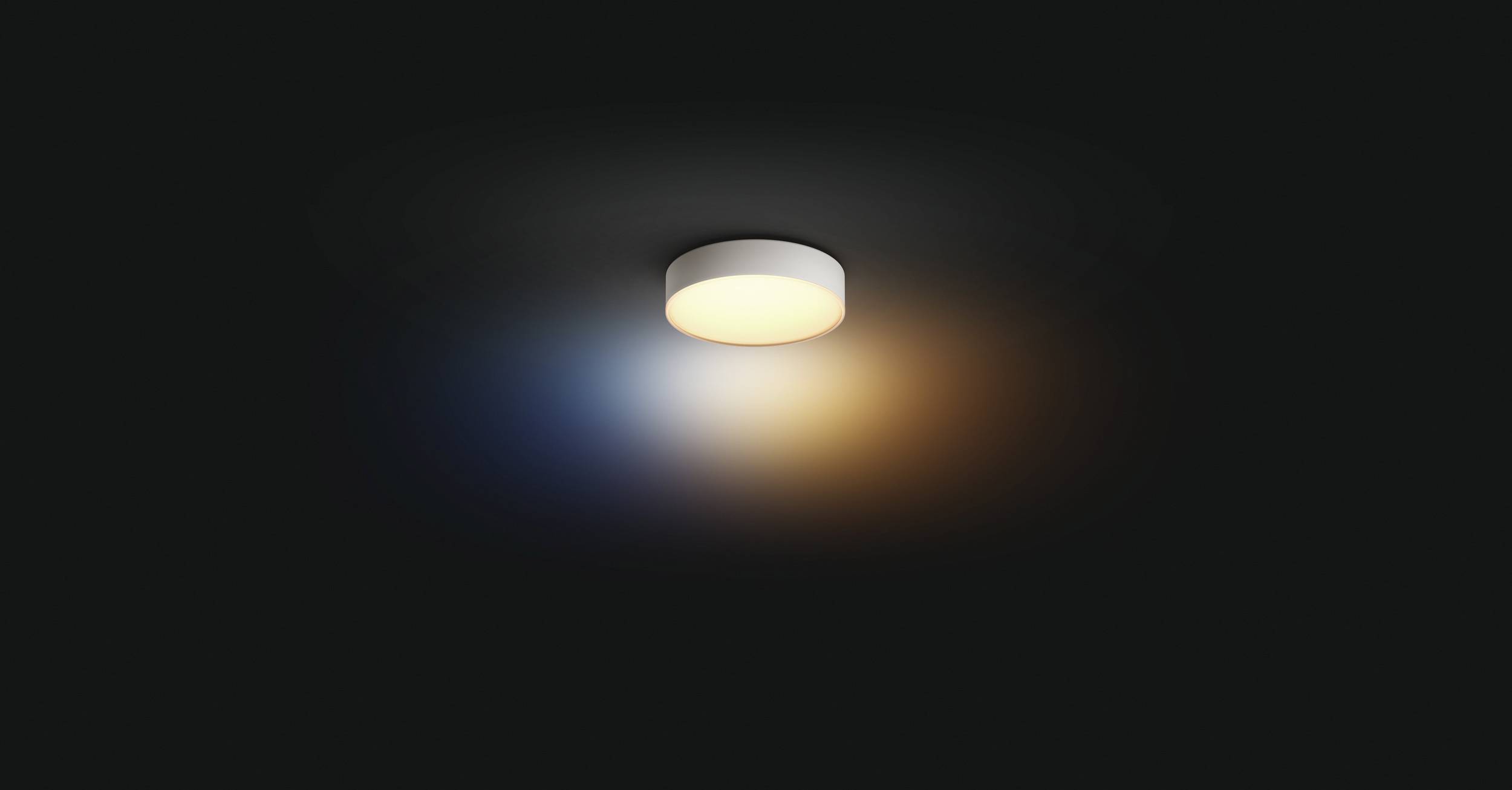 Een ronde plafondlamp straalt warmwit licht uit dat naar buiten toe overgaat in blauw en oranje, tegen een donkere achtergrond.
