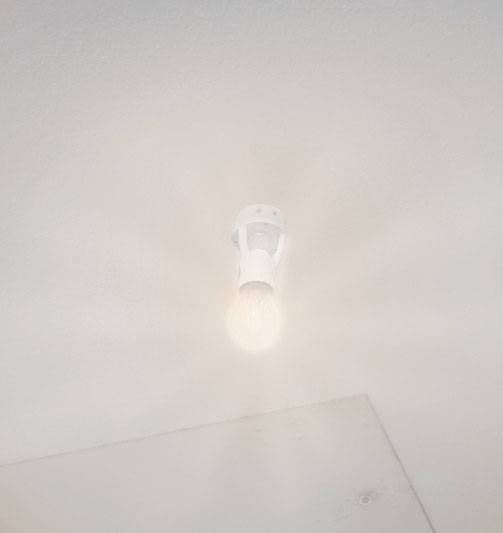 Een ingeschakelde gloeilamp aan het plafond straalt warm licht uit en creëert een subtiele lichtgloed.