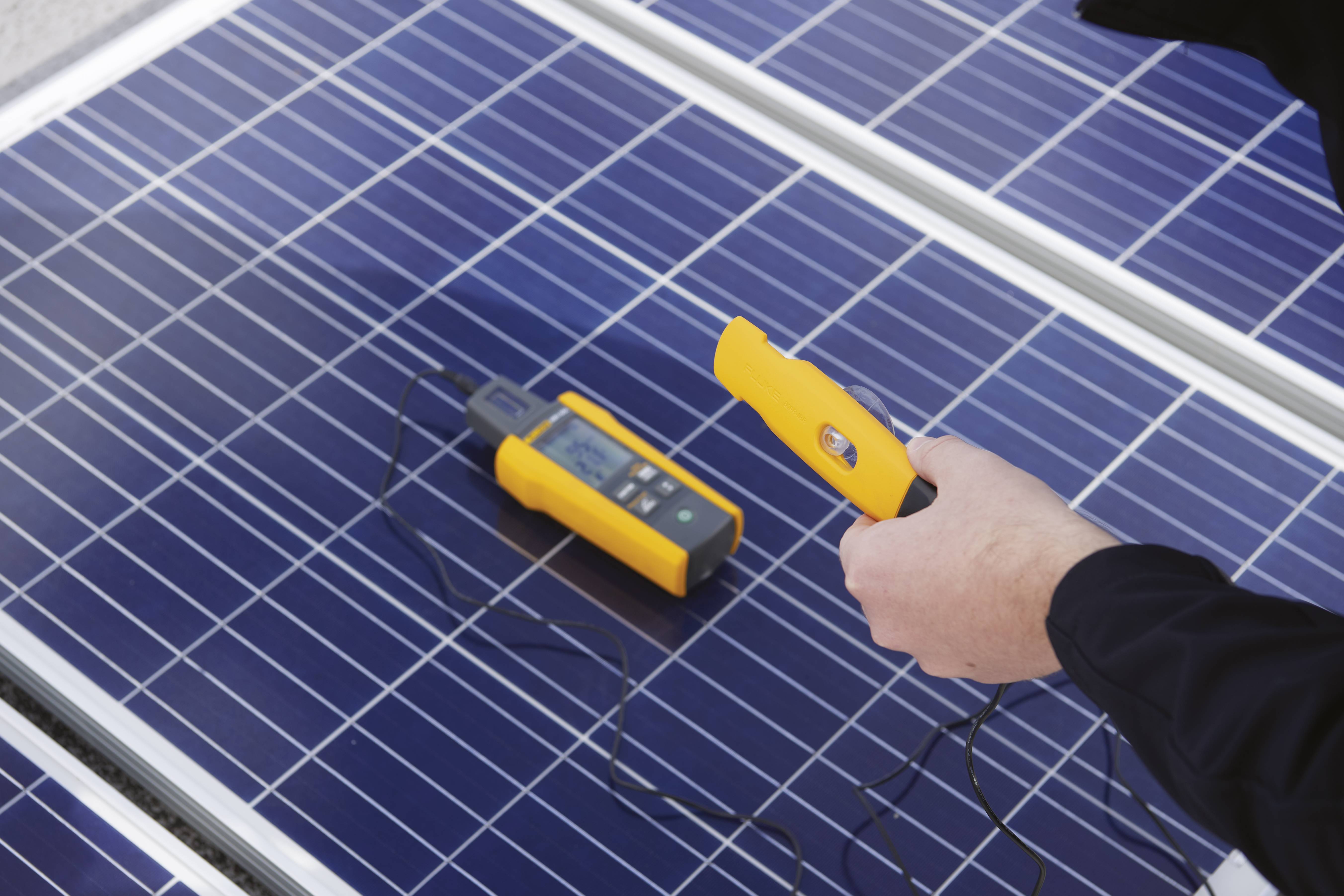 Een persoon houdt een meetinstrument boven een zonnepaneel om de prestaties van zonne-energie te controleren.