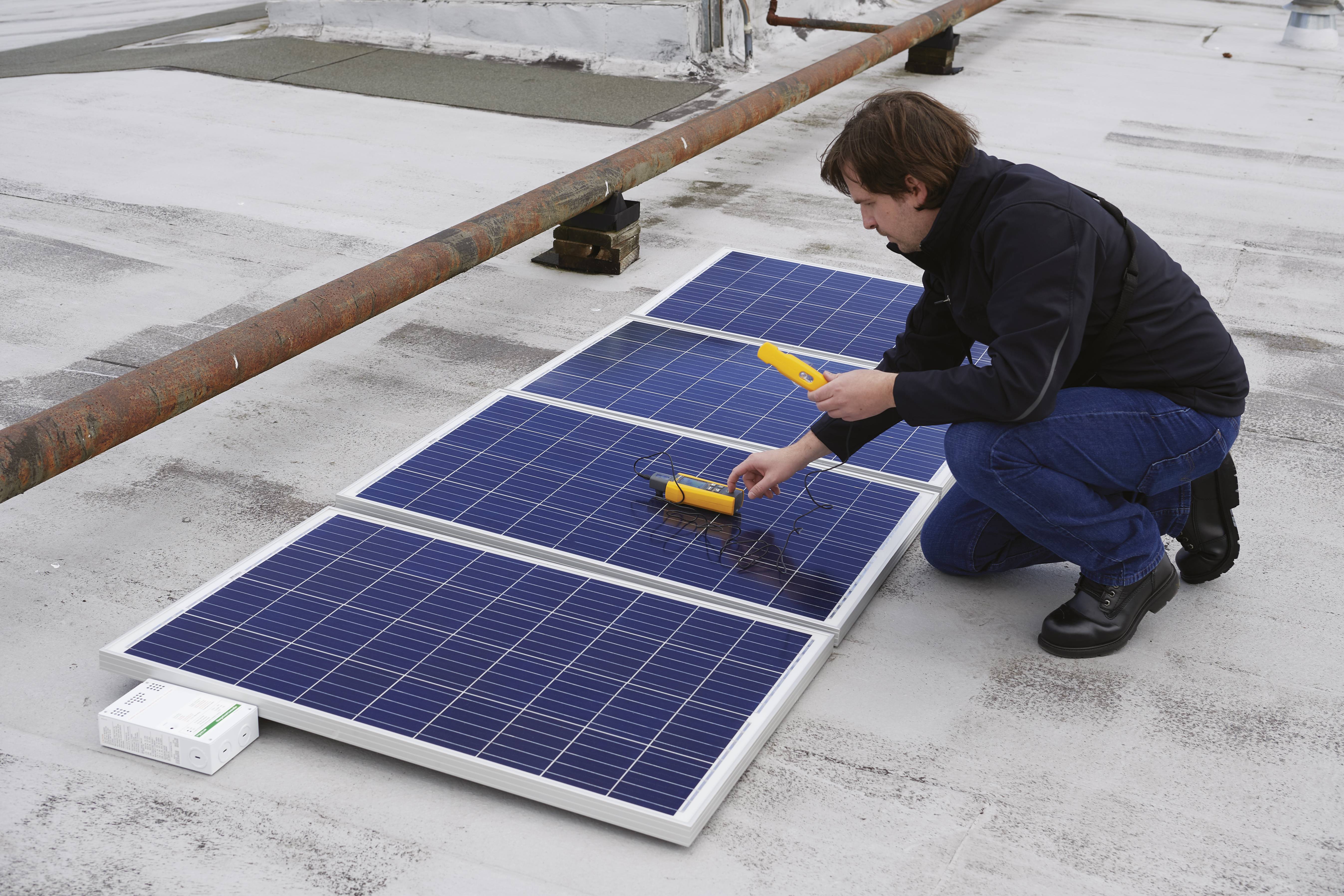 Een persoon controleert zonnepanelen op een plat dak met een meetapparaat.