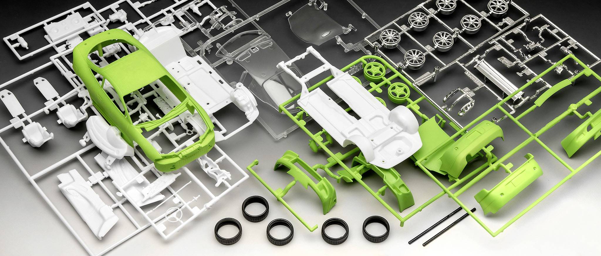 'Modelauto-kit met groene en witte autoonderdelen, wielen en montagehandleiding. Onderdelen zijn gerangschikt in aparte frames.'