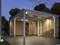 Een moderne carport met houten zijbekleding, 's nachts verlicht. Links is een stapel hout zichtbaar onder de overkapping.