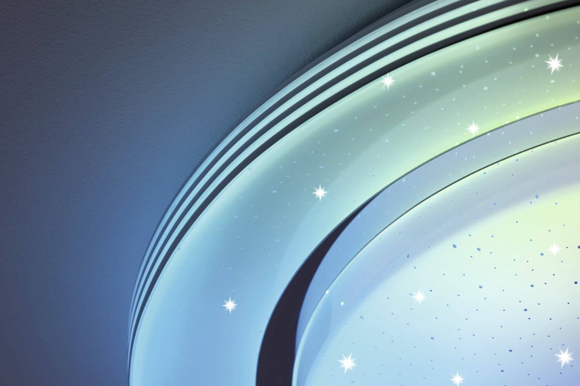 Halfbolvormige lamp met blauw-groene gloed en kleine puntlichtjes die eruitzien als sterren, aan een muur bevestigd.