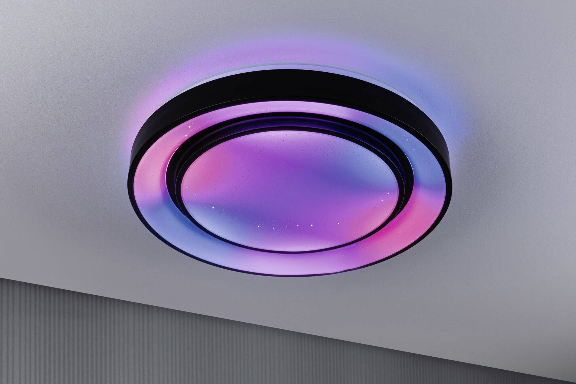 Moderne plafondlamp die in verschillende kleuren oplicht, variërend van roze tot blauw, geïnstalleerd aan een witte plafond.