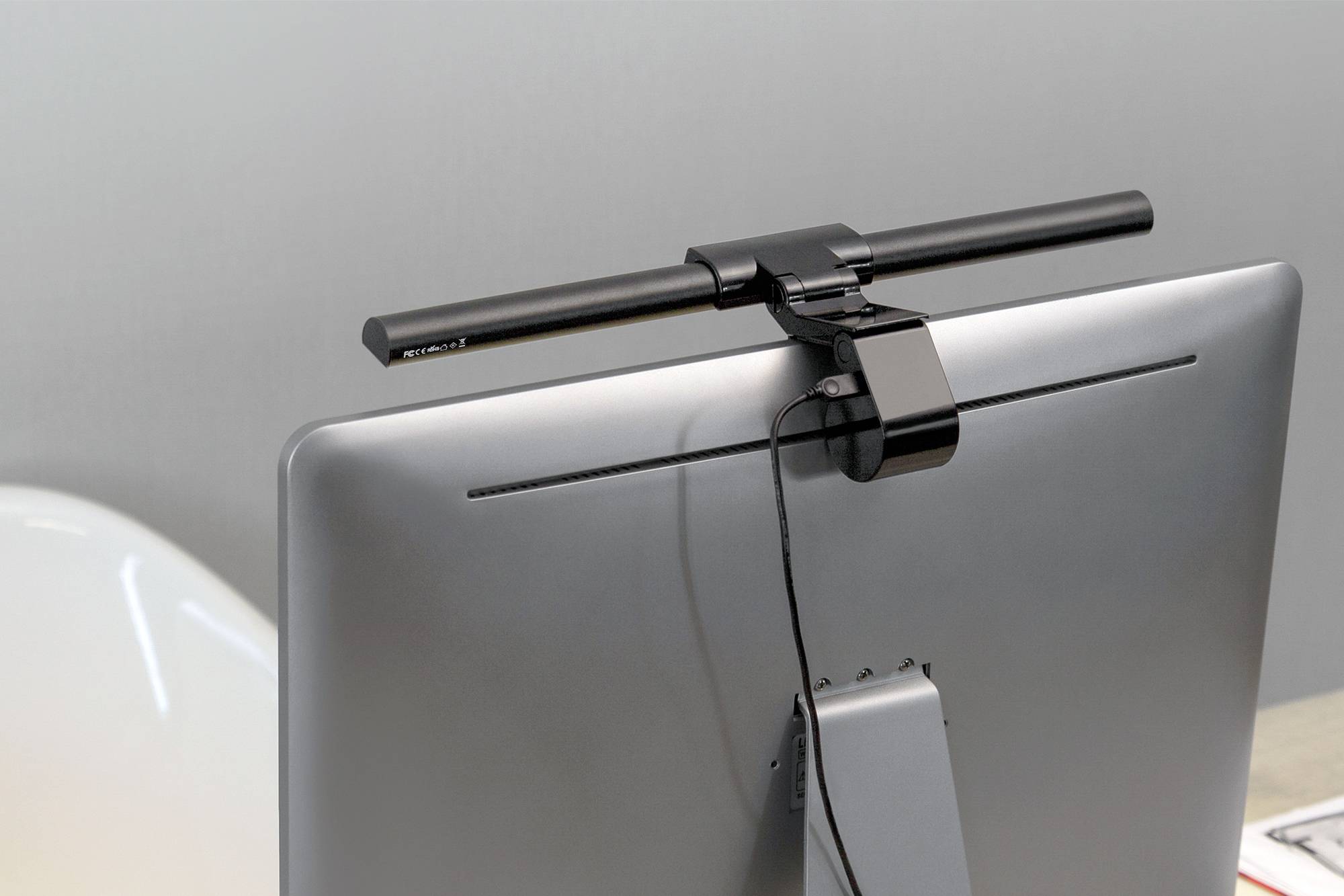 Een zwarte LED-lamp is bovenaan een computerscherm bevestigd. Hij verlicht de werkruimte van bovenaf.