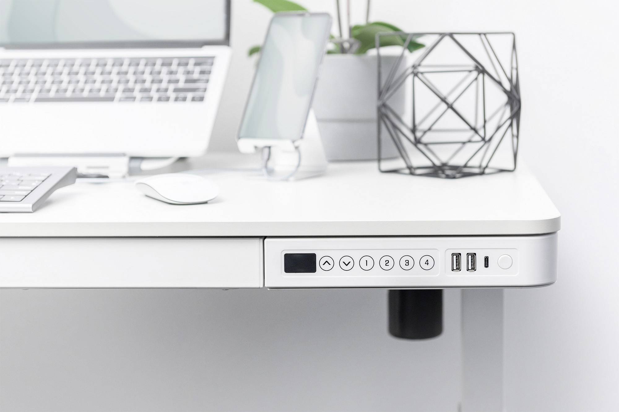 Een moderne, witte bureau met verstelbaar bedieningspaneel, met daarop een laptop, smartphonestandaard en geometrische decoratie.