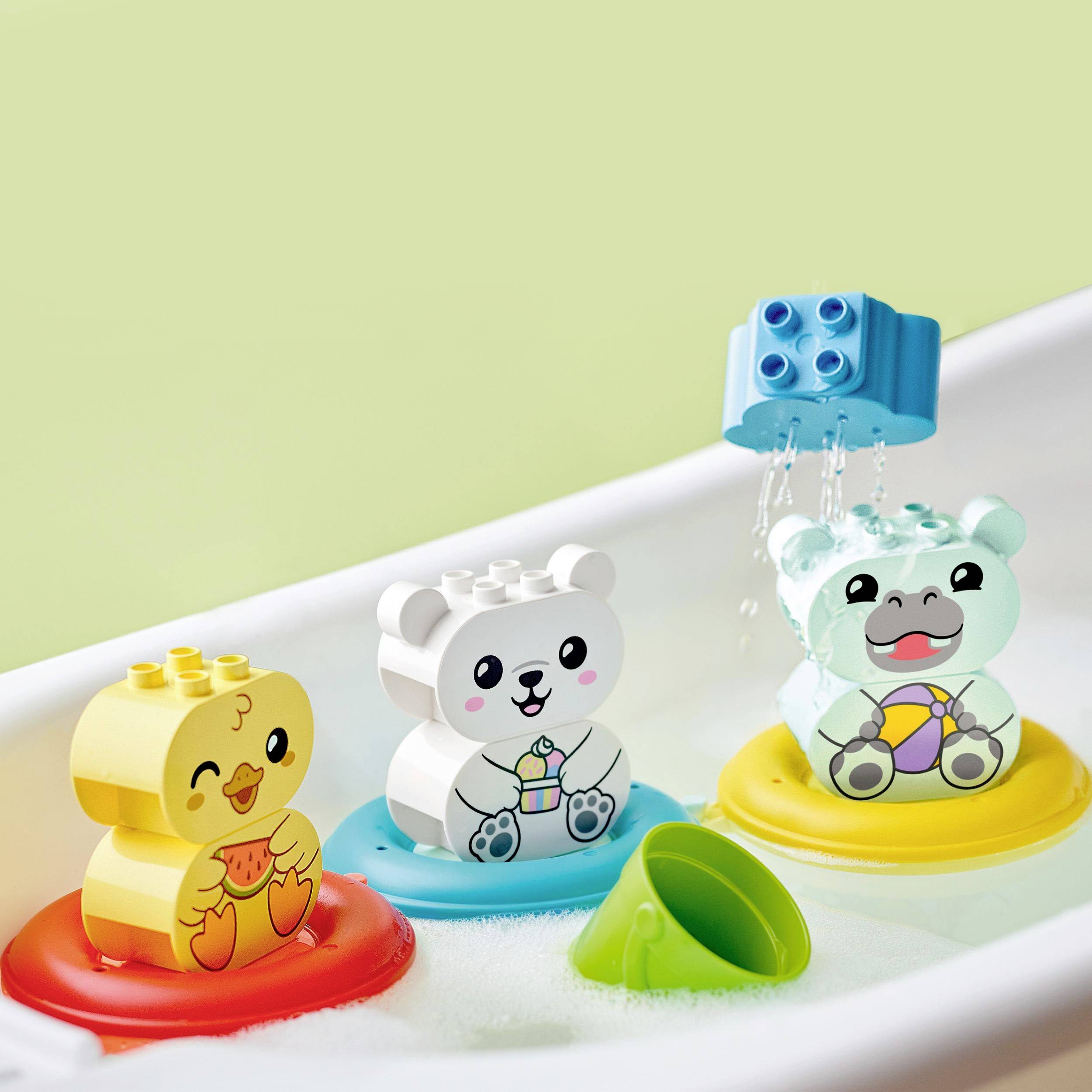 Drie kleurrijke, drijvende speelgoedfiguren - een eend, een beer en een nijlpaard - in een badkamer, met zeepbellen en een watersproeier.
