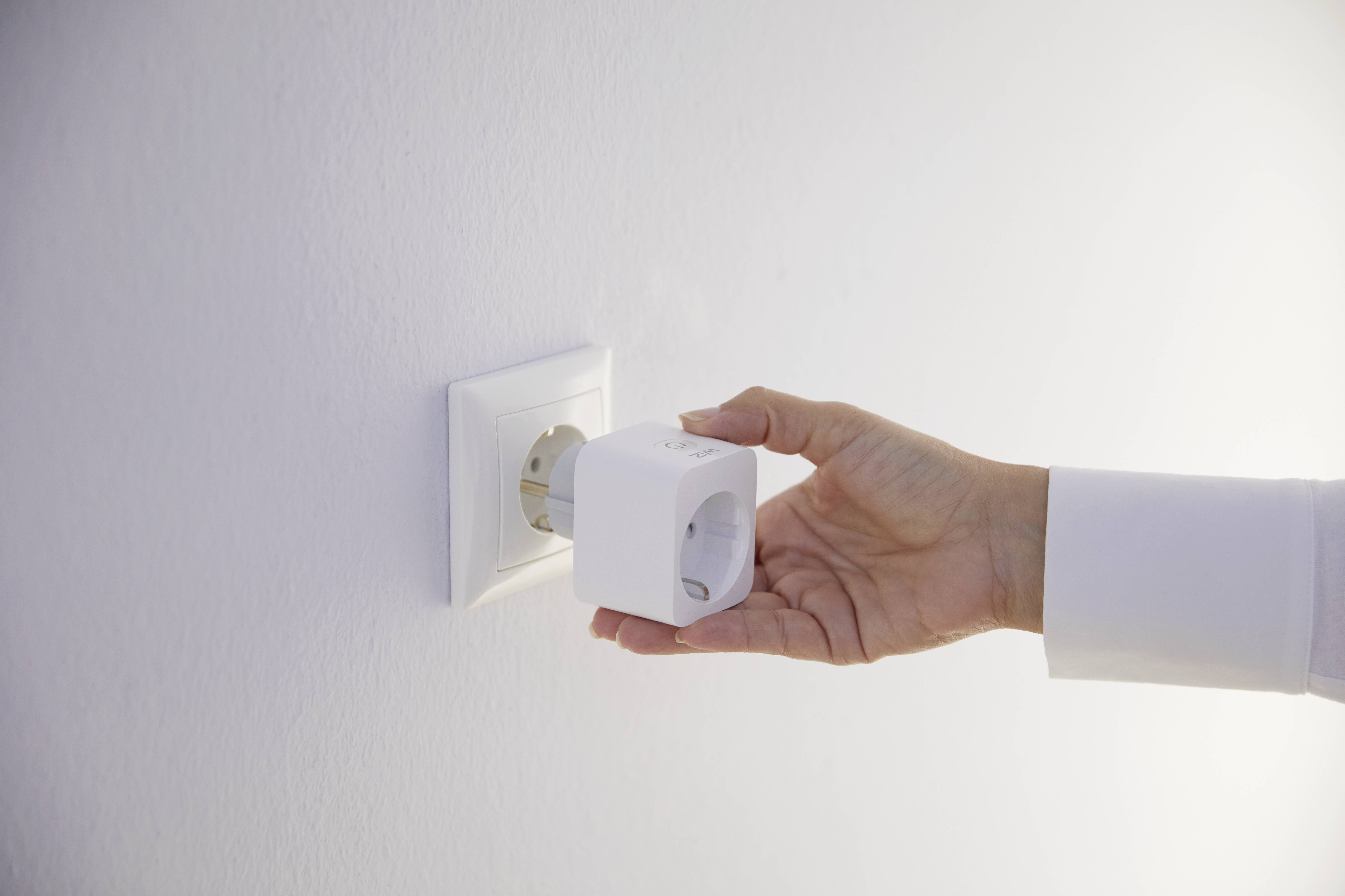 Een hand steekt een witte adapter in een wandcontactdoos.
