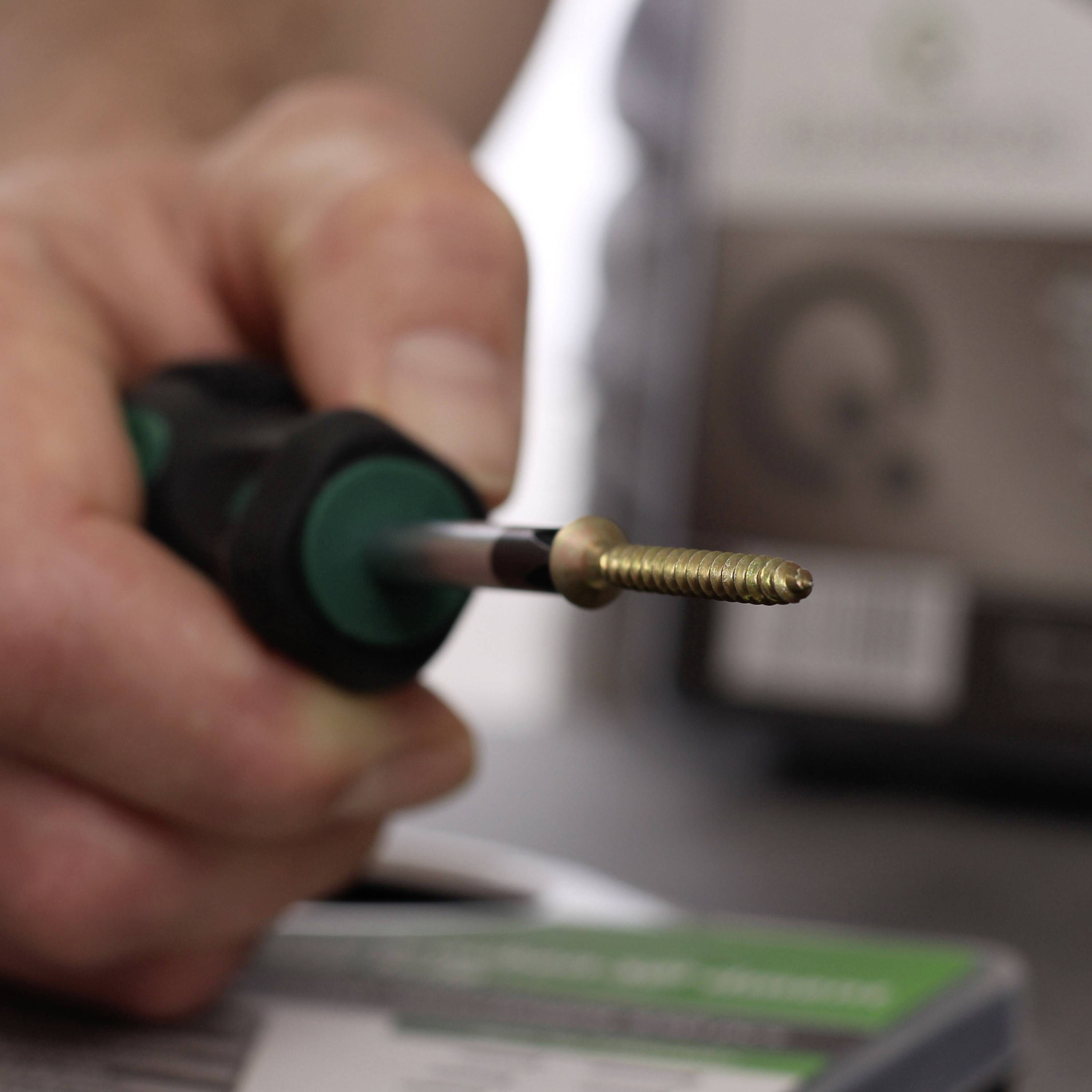 Hand houdt schroevendraaier vast met gouden schroef, onscherpe achtergrond. Focus op schroef en gereedschap, uitvindersvernuft wordt gesuggereerd.