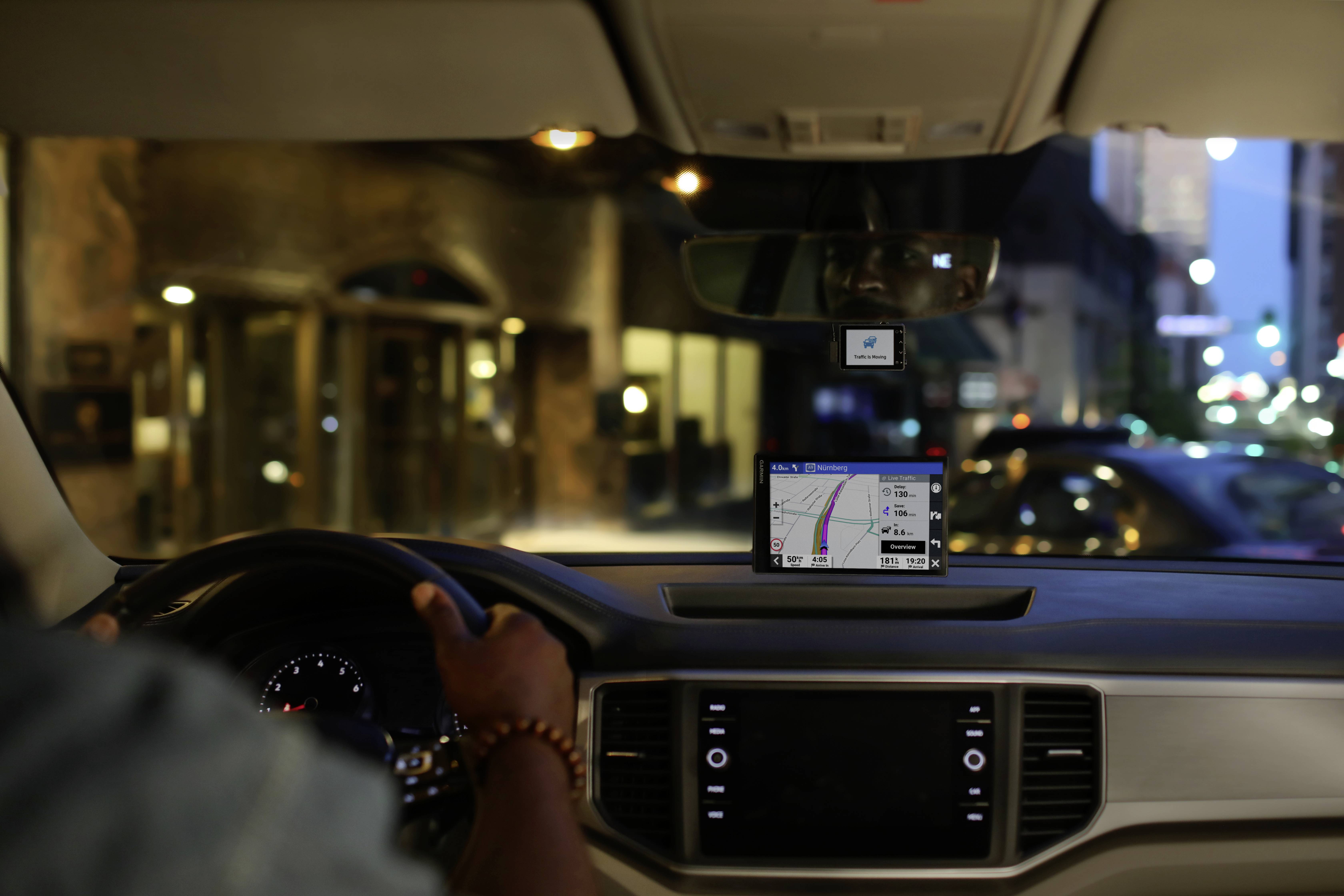 Een automobilist navigeert 's nachts door een stadsstraat met een gps-systeem op het dashboard. Lichten en gebouwen zijn op de achtergrond zichtbaar.