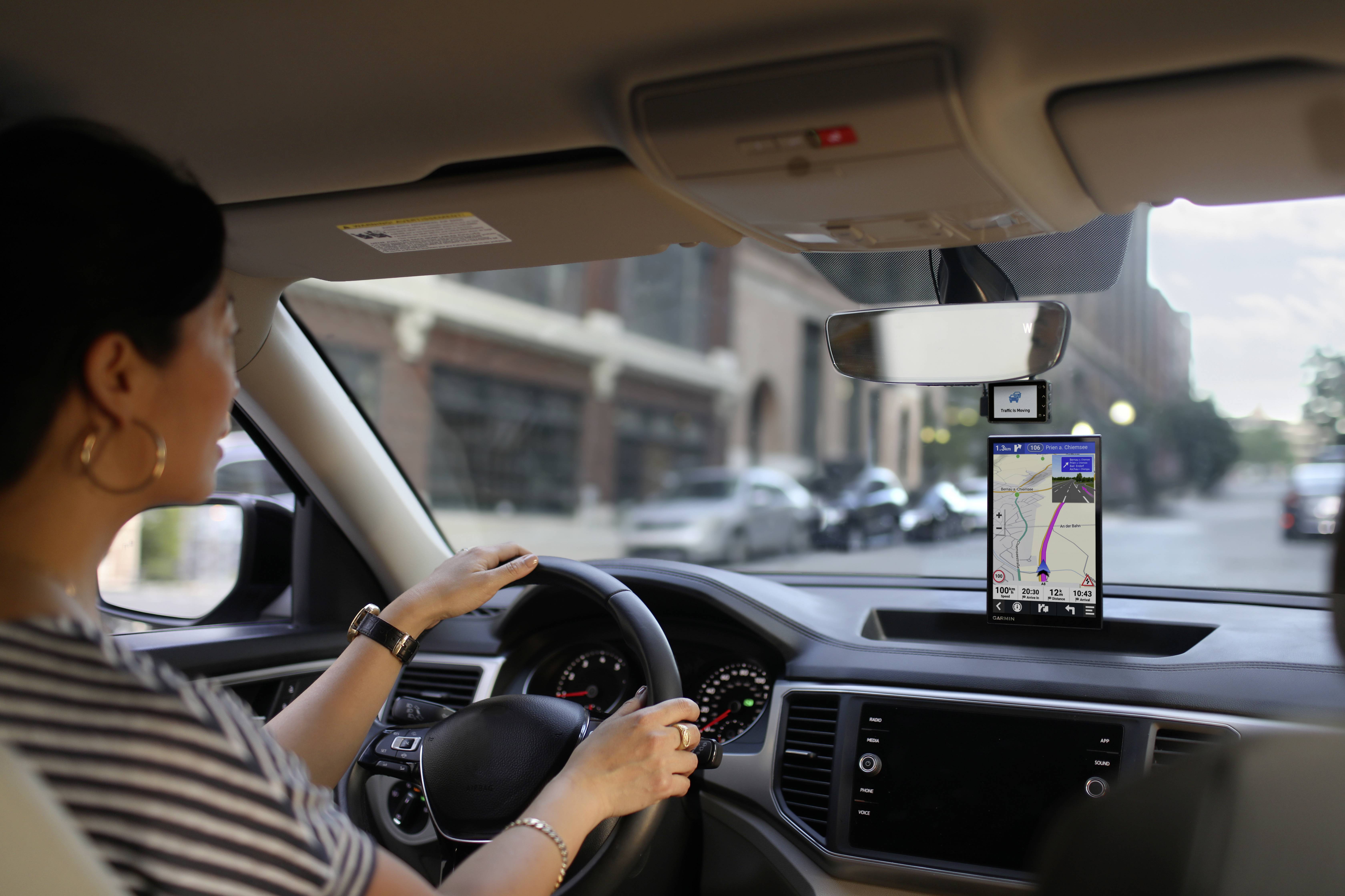 Een vrouw rijdt een auto in een stad en volgt de aanwijzingen van een navigatiesysteem op haar telefoon, die is bevestigd aan de voorruit.