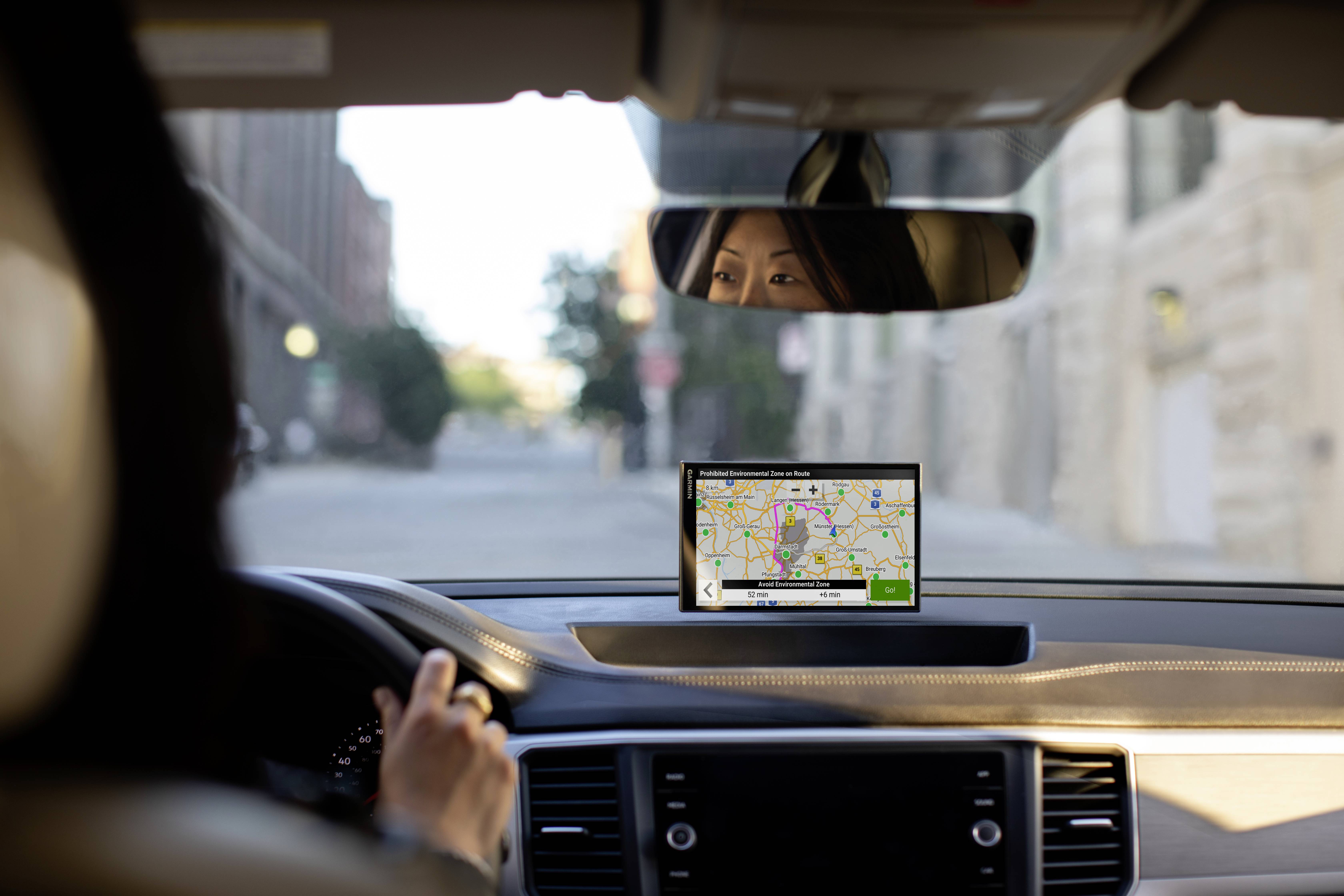 Een persoon rijdt een auto in een stedelijke omgeving. Een navigatieapparaat op het dashboard toont een stadskaart en een route.