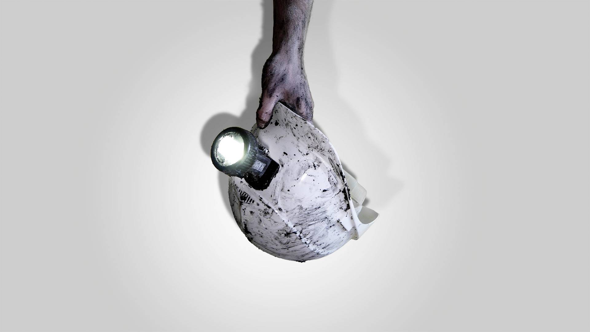 Een hand houdt een vuile bouwhelm vast met een brandende zaklamp erop.