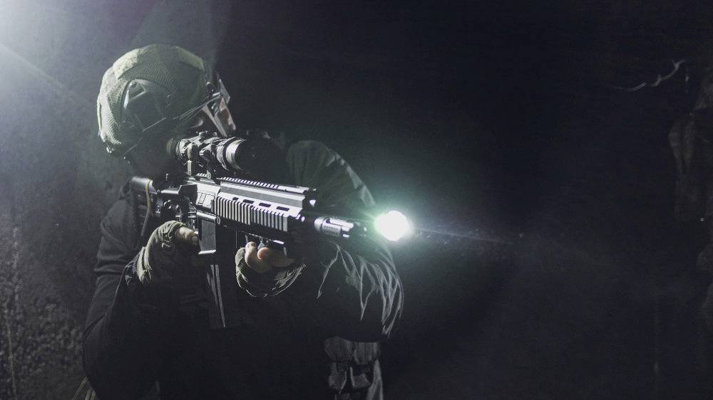 Soldaat in camouflage-uitrusting richt een geweer in een donkere ruimte, met een zaklamp bevestigd. Geconcentreerde gezichtsuitdrukking, dramatische verlichting.
