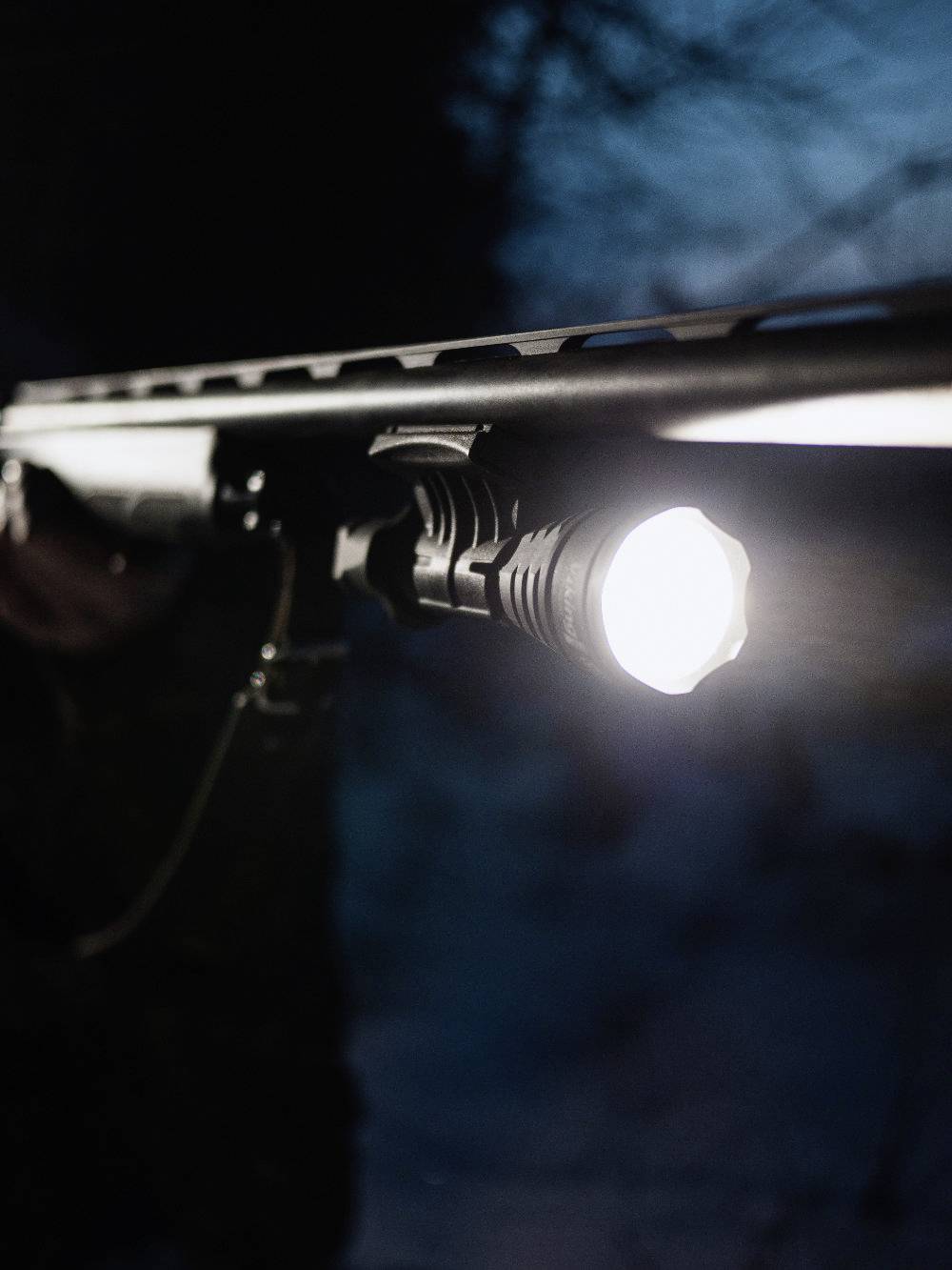 Een geweer met een bevestigde zaklamp die schijnt in een donkere omgeving.