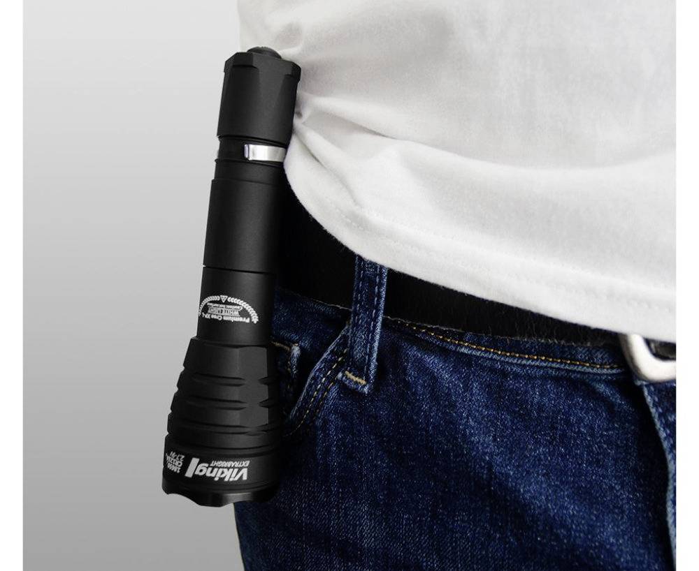 Een zwarte zaklamp is bevestigd aan de riem van een persoon in spijkerbroek en een wit shirt.