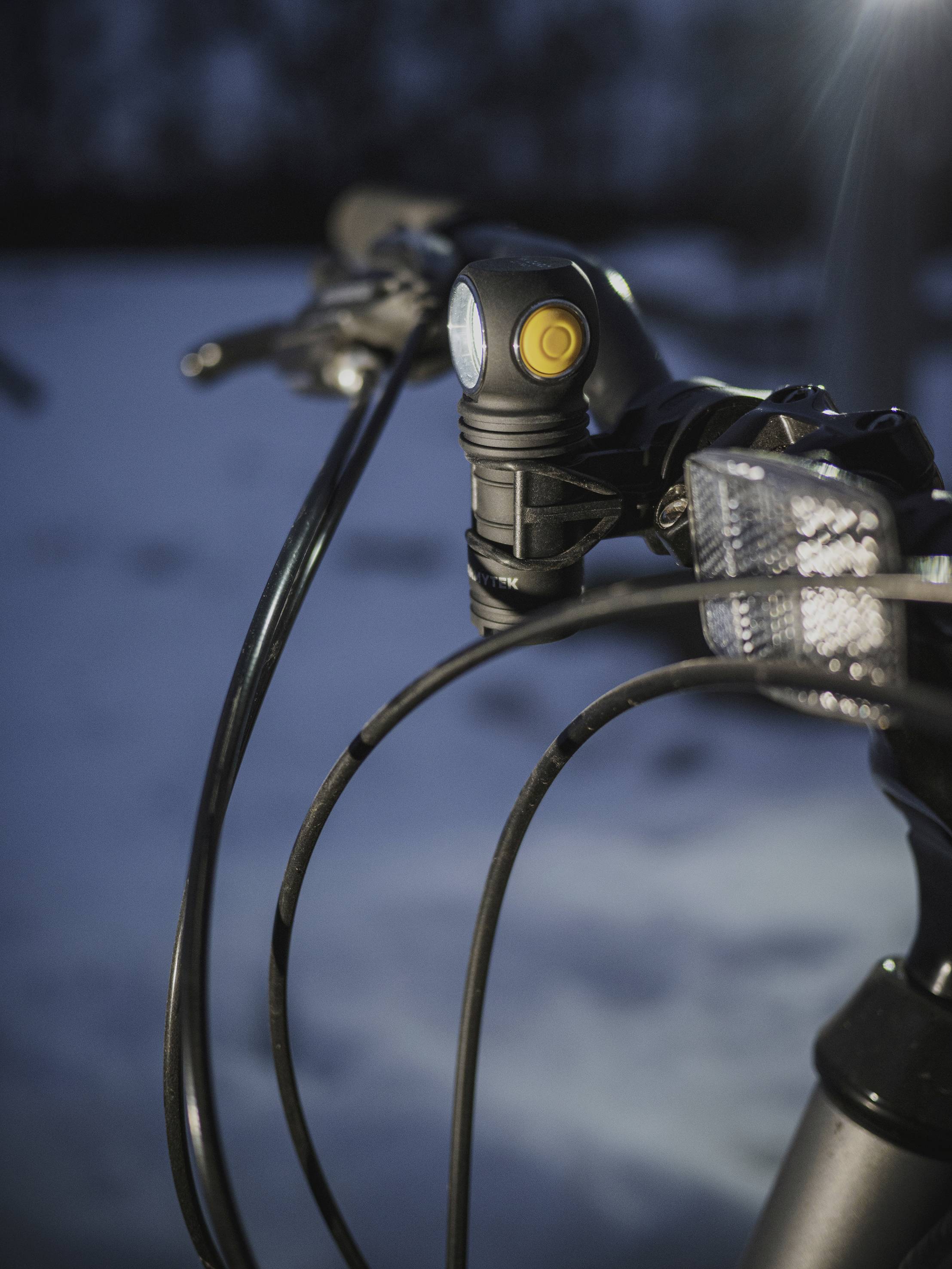 Close-up van een fiets met een verlicht voorlicht in het donker. De sneeuw op de achtergrond wijst op een winterlijke omgeving.