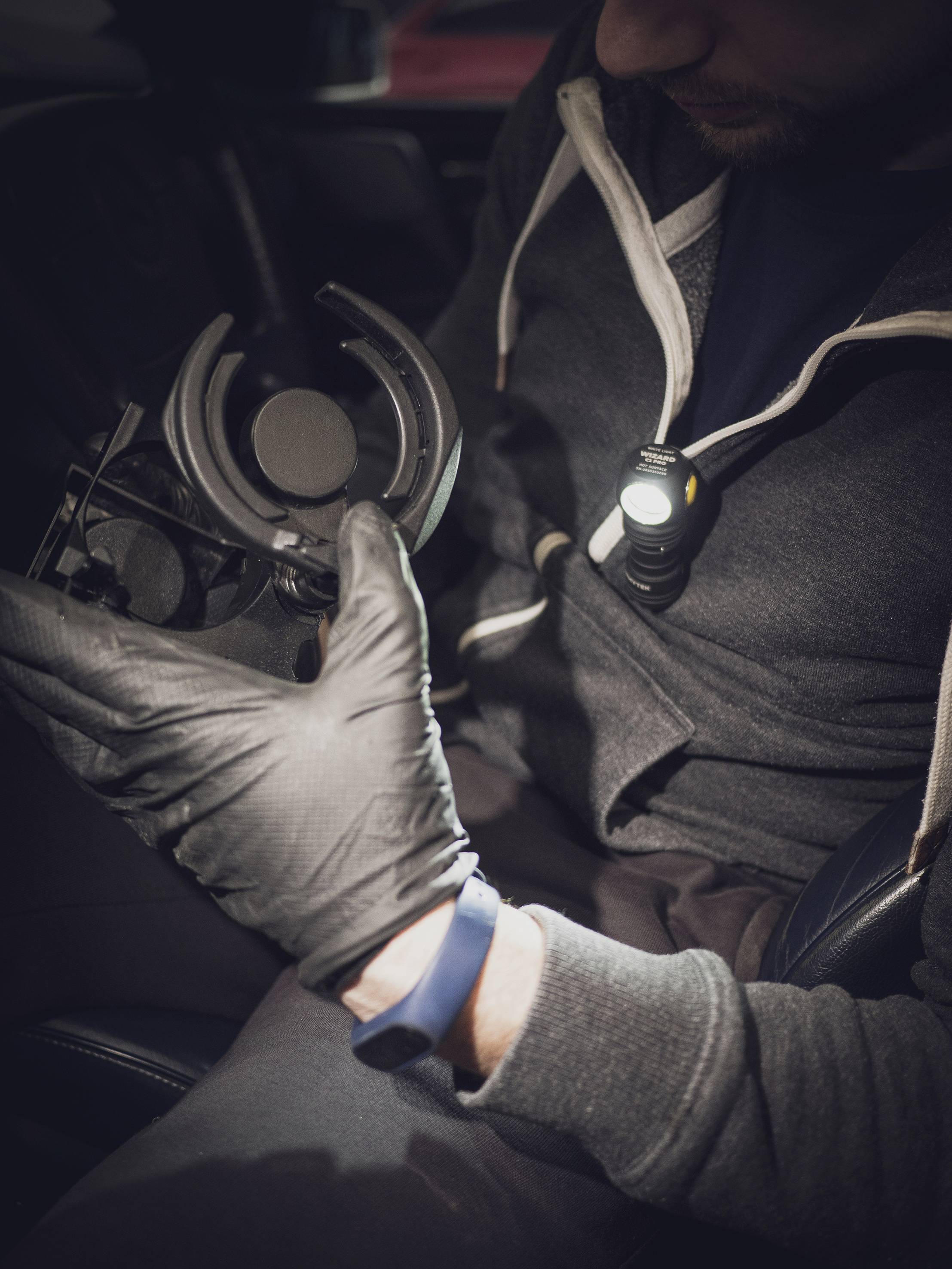 Een persoon in werkkleding repareert een technisch apparaat, draagt zwarte handschoenen en gebruikt een hoofdlamp om beter te kunnen zien.