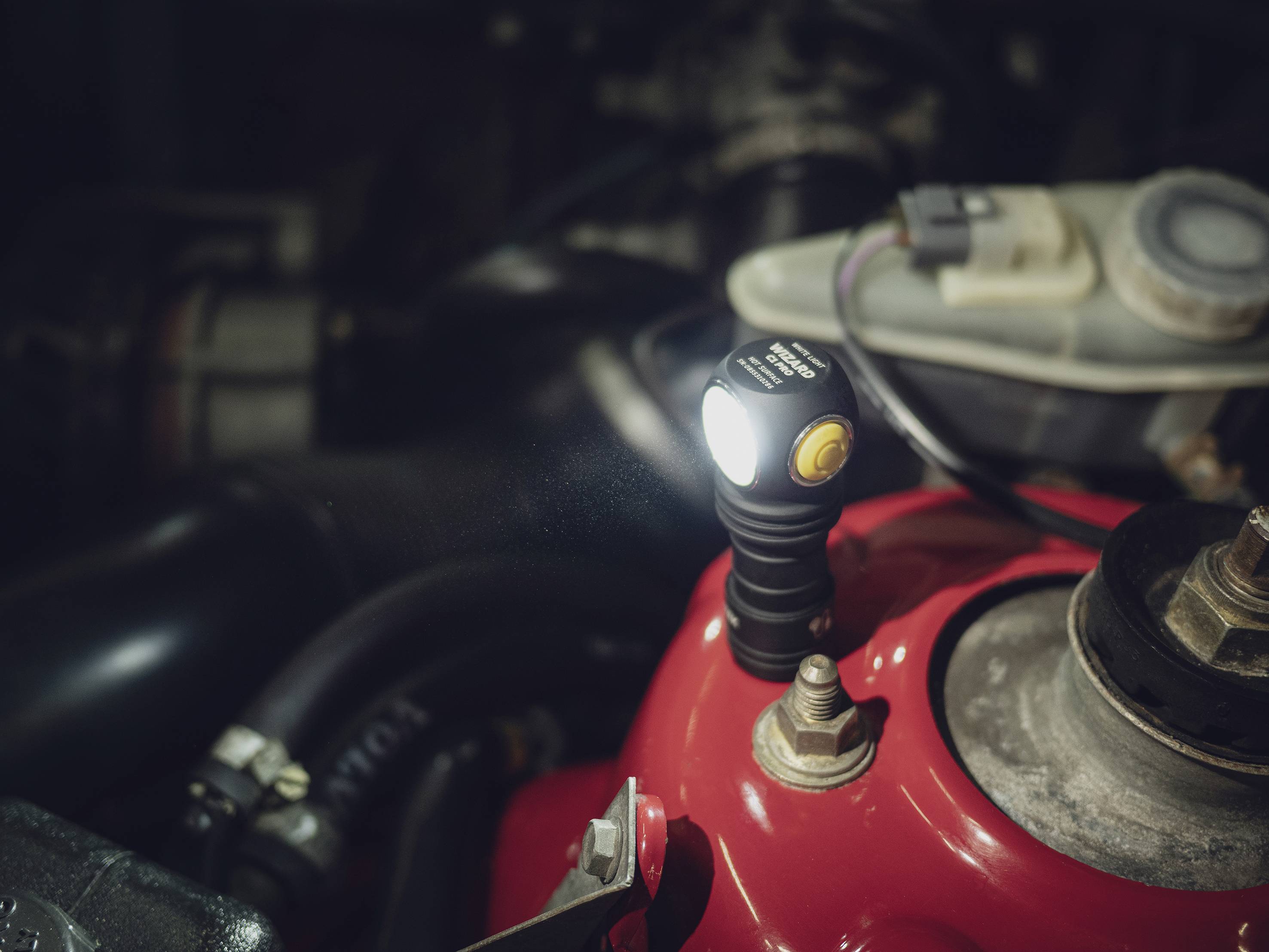 Close-up van een motorruimte met een felle LED-zaklamp die is bevestigd op een rood onderdeel.