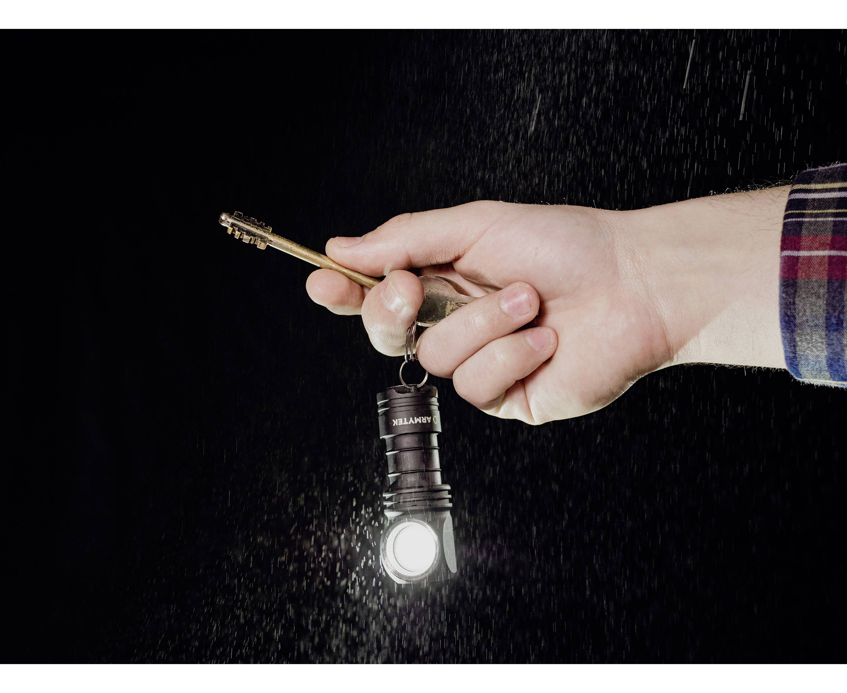 Een hand houdt een kleine, lichtgevende zaklamp in een donkere ruimte. De lamp hangt aan een sleutel.