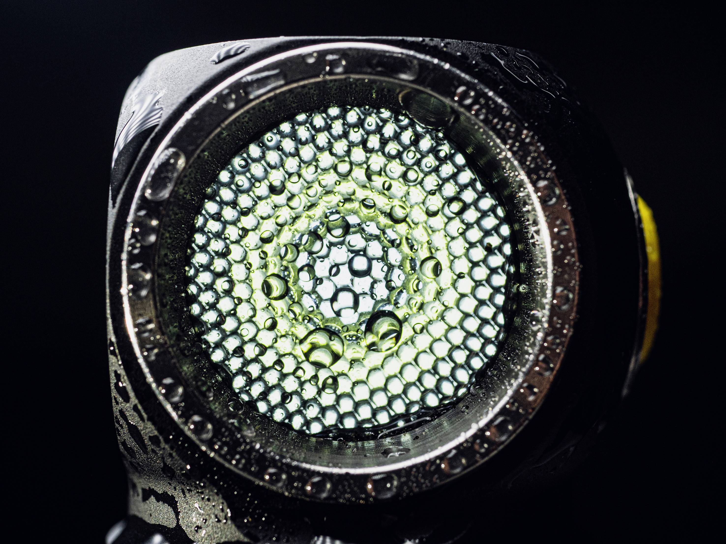 'Close-up van een natte zaklantaarnlens met honingraatpatroon en condenswater'