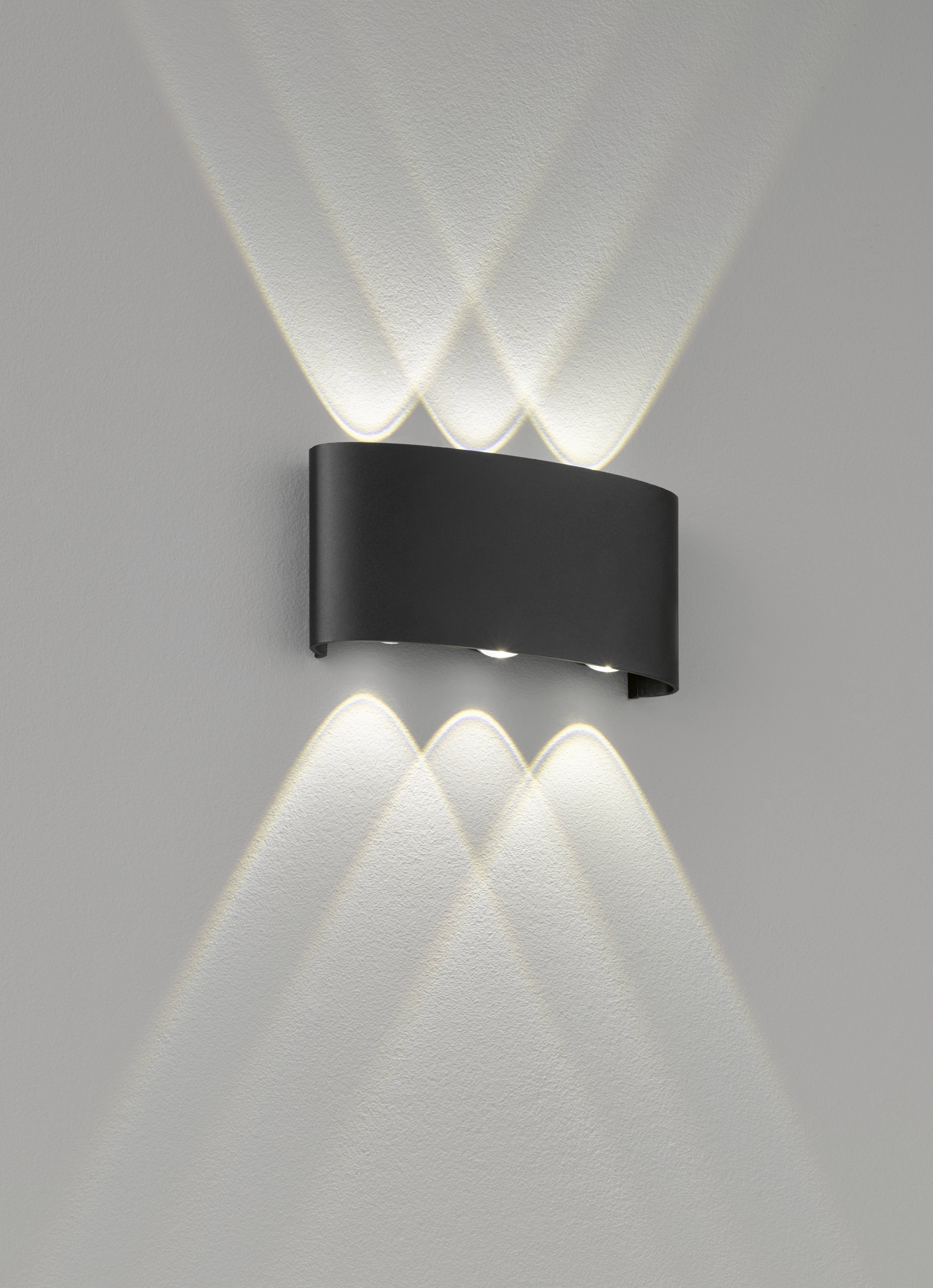 Een zwarte wandlamp straalt licht naar boven en beneden, creëert een stijlvol patroon van lichtstralen op de muur.