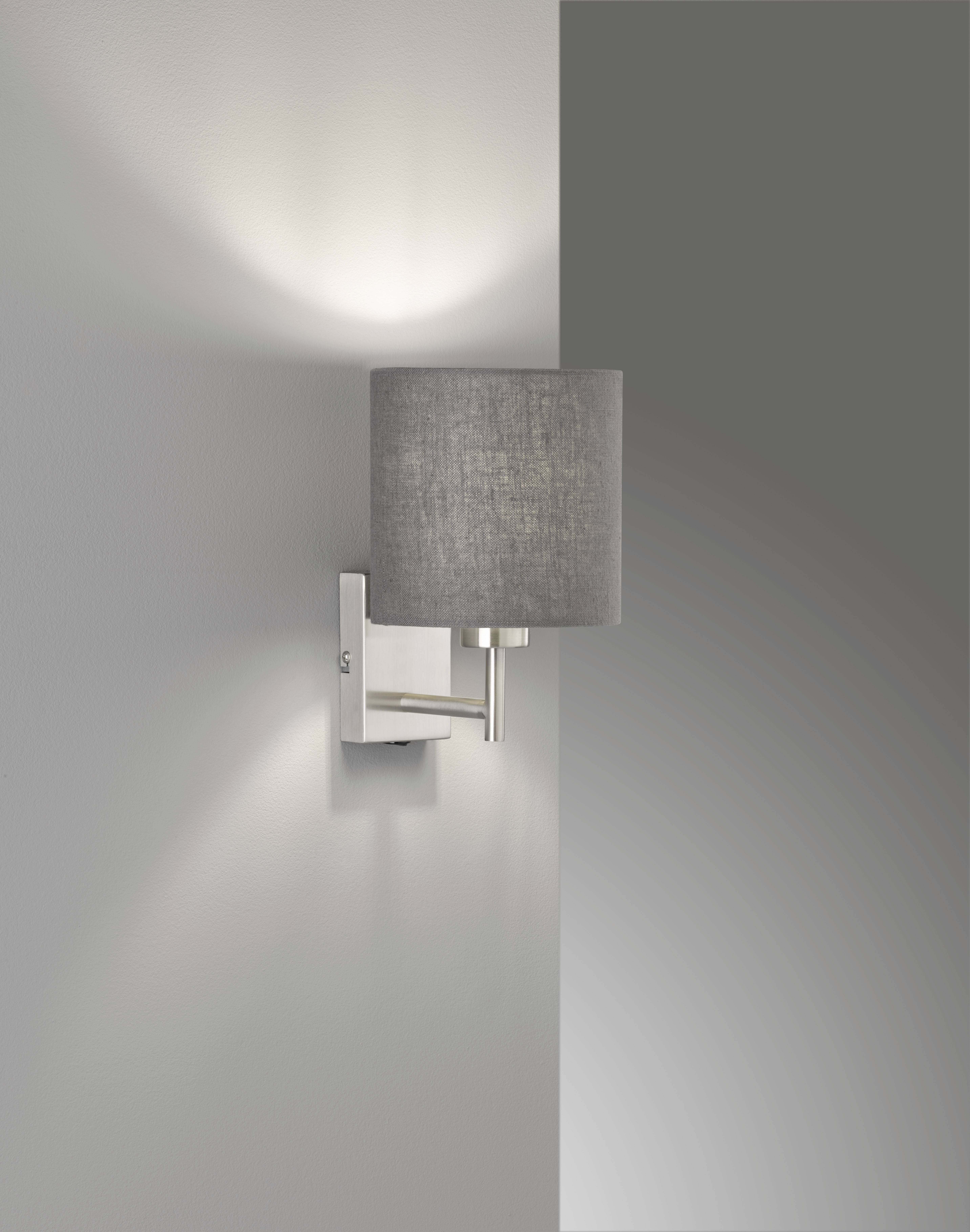 Een moderne wandlamp met een grijze stoffen lampenkap verspreidt warm licht tegen een grijze muur, waardoor een zachte sfeer ontstaat.