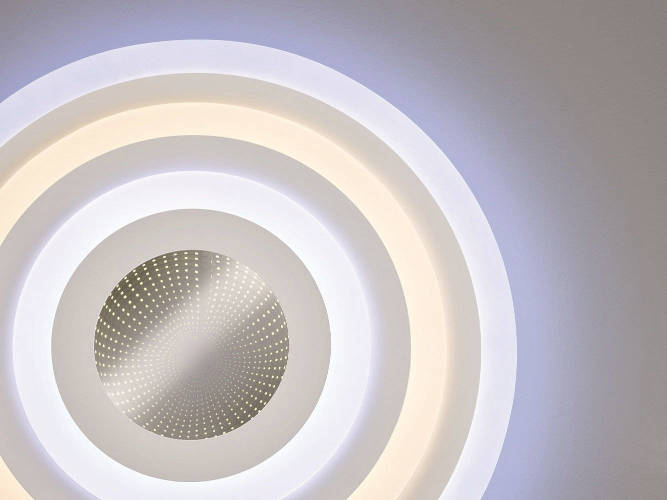 Ronde plafondlamp met concentrische lichtringen die van warm naar koel wit overgaan en een moderne uitstraling hebben.