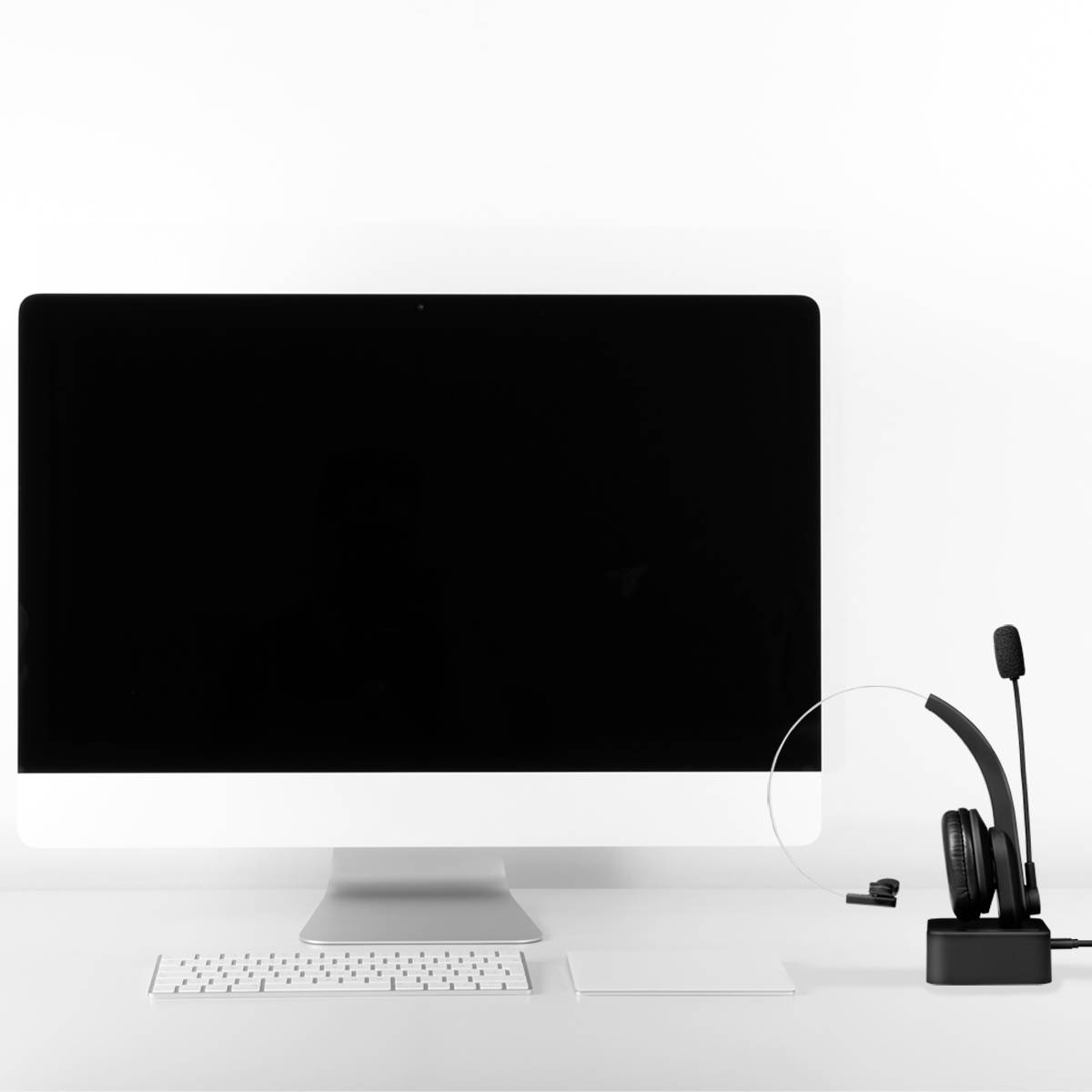Een bureau met een grote monitor, een wit toetsenbord, een wit vel papier en een headset op een standaard.