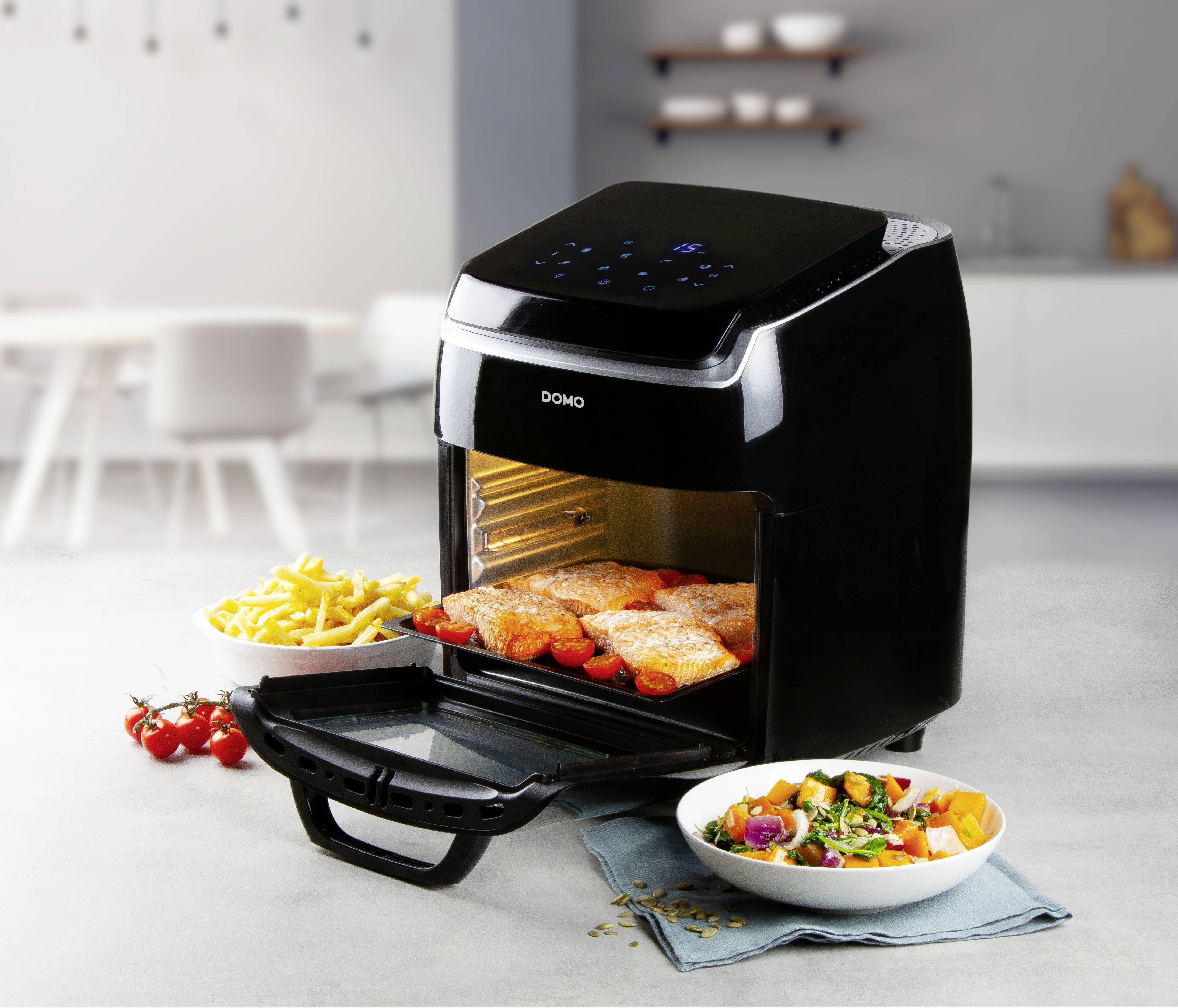 Een zwarte Airfryer van DOMO staat op een keukentafel. Hij is geopend en bevat stukken kip en groenten. Ernaast een kom met salade en een met friet.