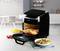 Een zwarte Airfryer van DOMO staat op een keukentafel. Hij is geopend en bevat stukken kip en groenten. Ernaast een kom met salade en een met friet.