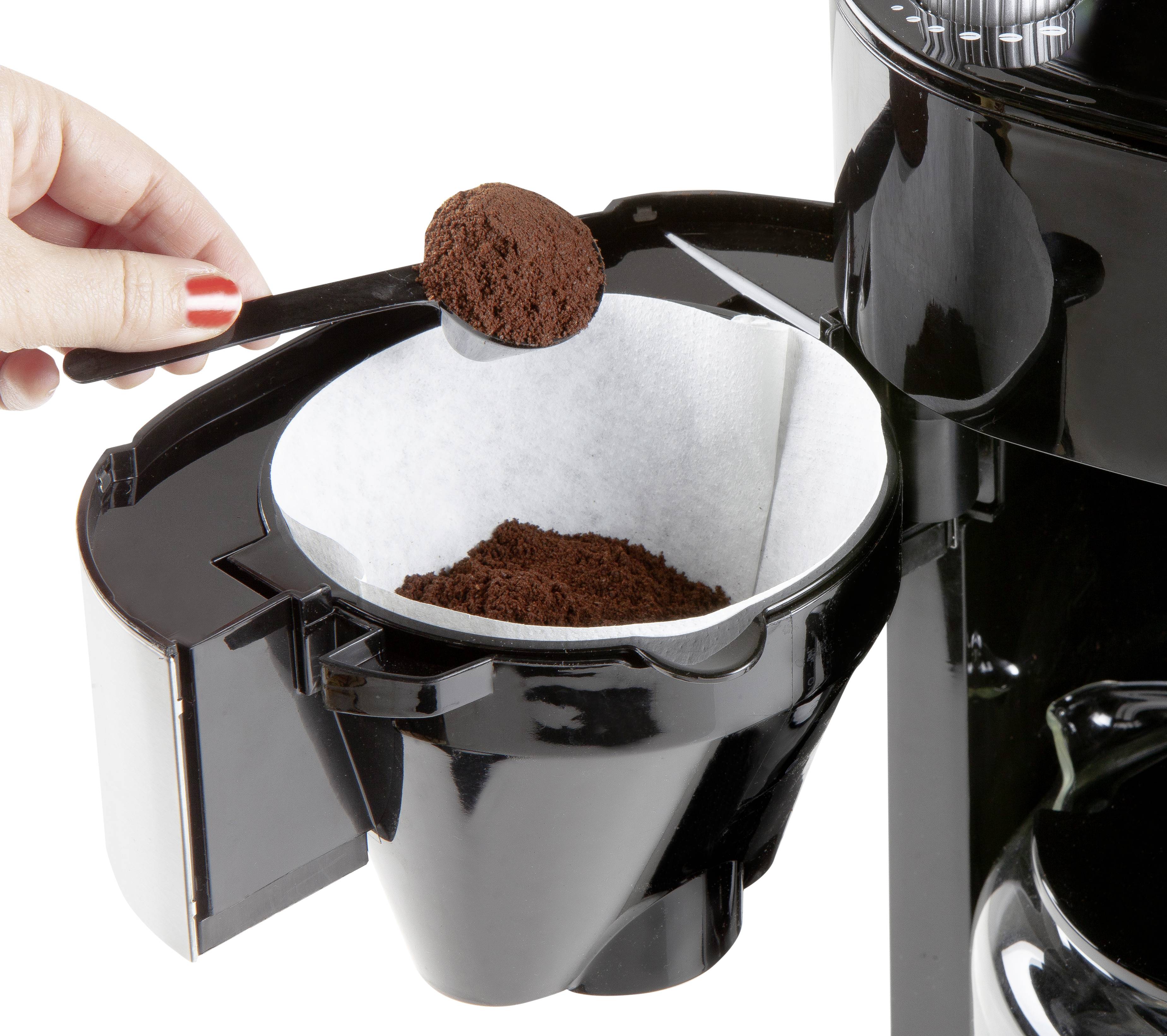 Een hand vult gemalen koffie met een maatlepel in het koffiefilter van een koffiemachine.