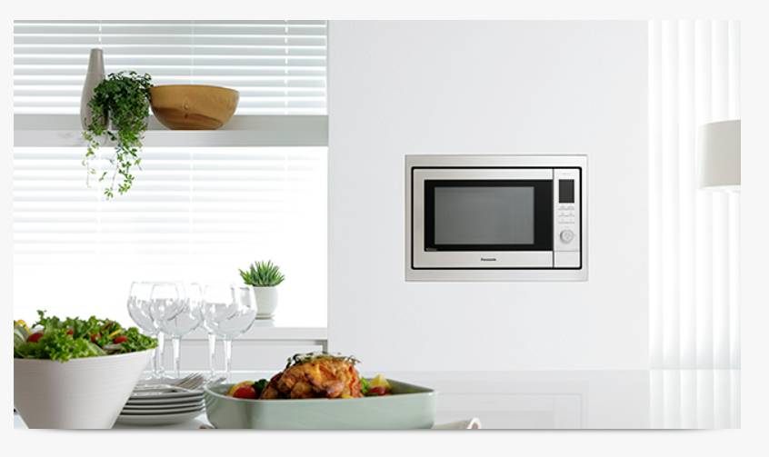 Een modern keukeninterieur met een ingebouwde magnetron in de muur. Op een tafel staan een gebraden kip en een salade.