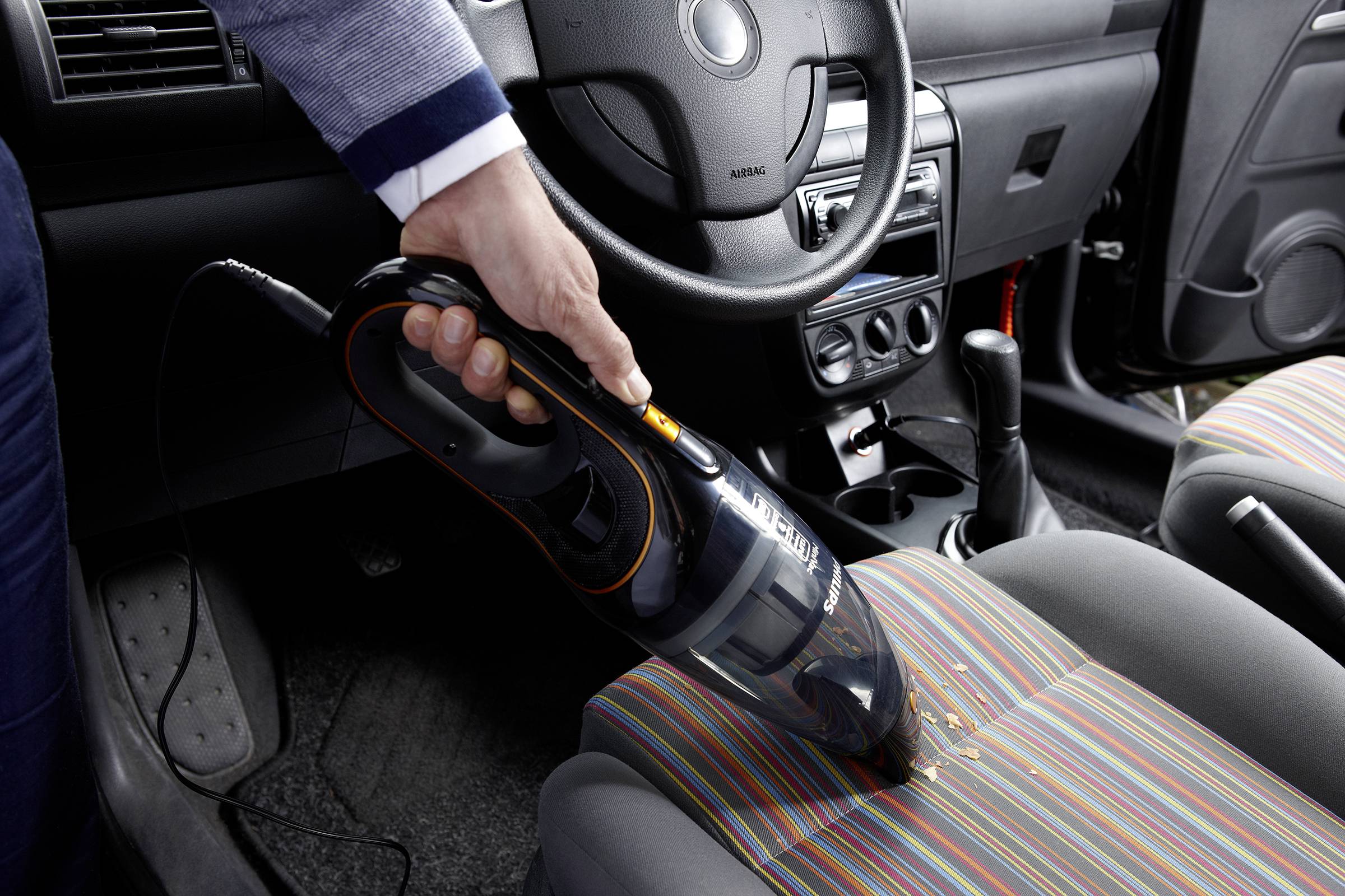 'Een persoon zuigt kruimels van de autostoel met een handstofzuiger.'