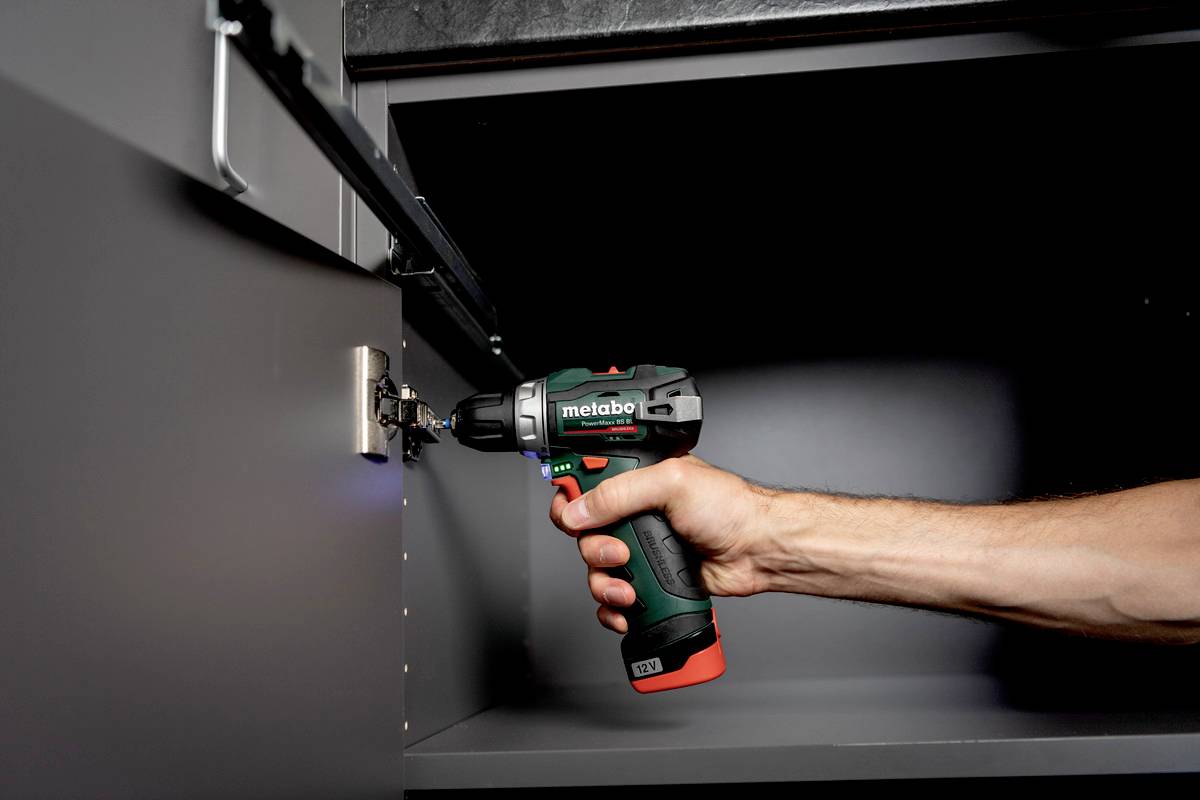 Een accuschroevendraaier wordt gebruikt om een scharnier aan een kast te bevestigen. Een hand houdt het gereedschap stevig vast.