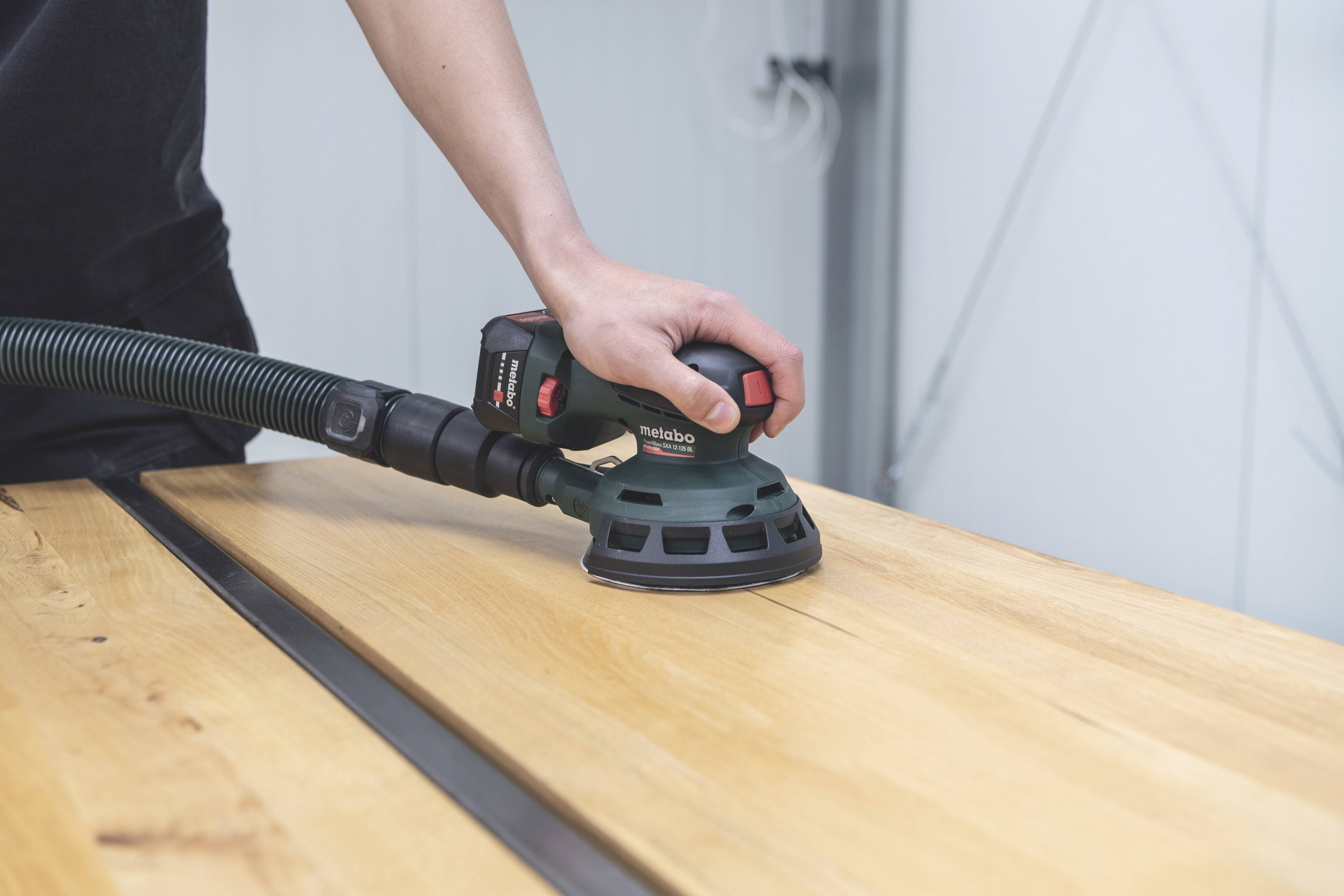 Een persoon schaaft een houten plaat met een elektrisch schuurapparaat in een werkplaats.