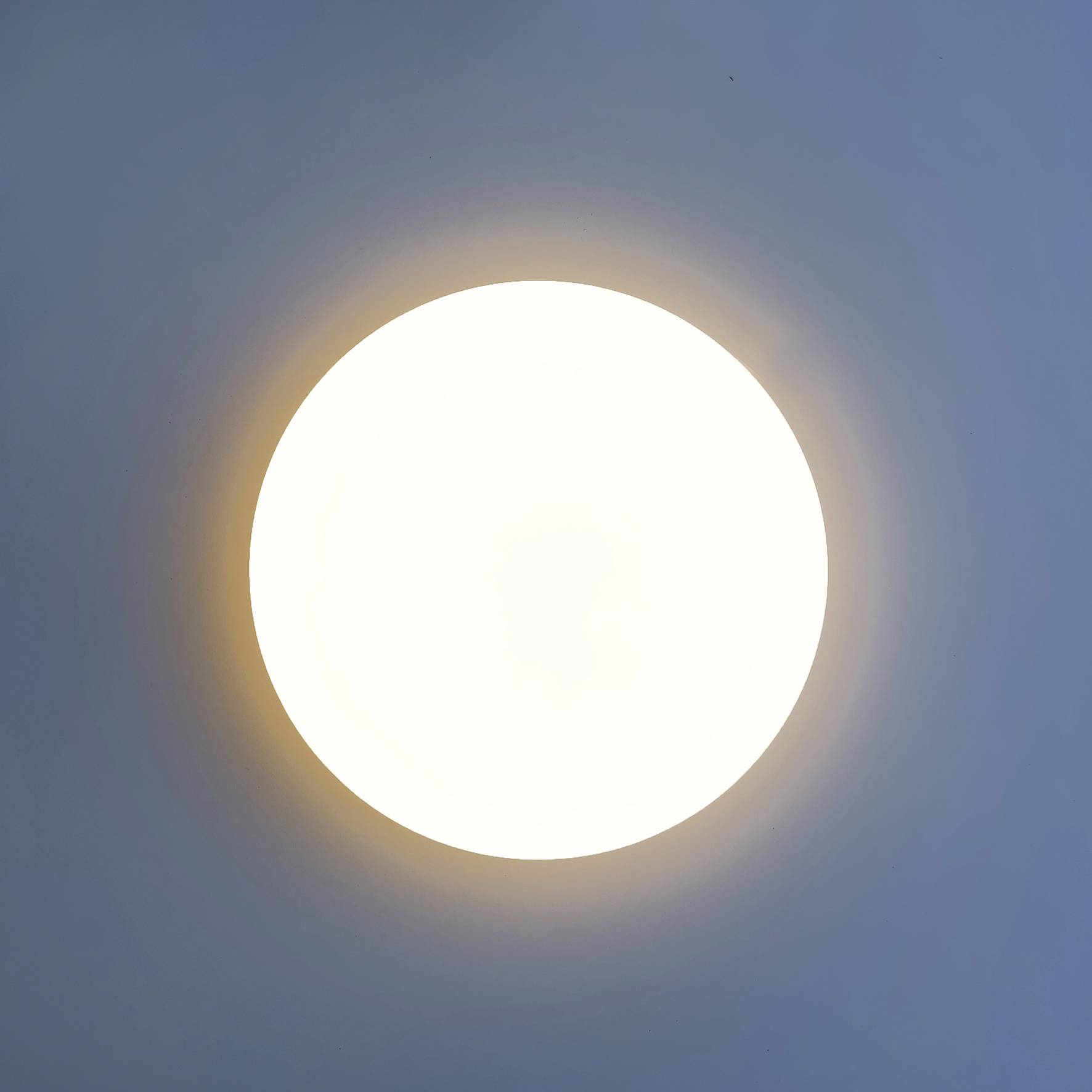 Een helder, rond lichtgevend oppervlak op een blauwe achtergrond dat doet denken aan een stralende zon.