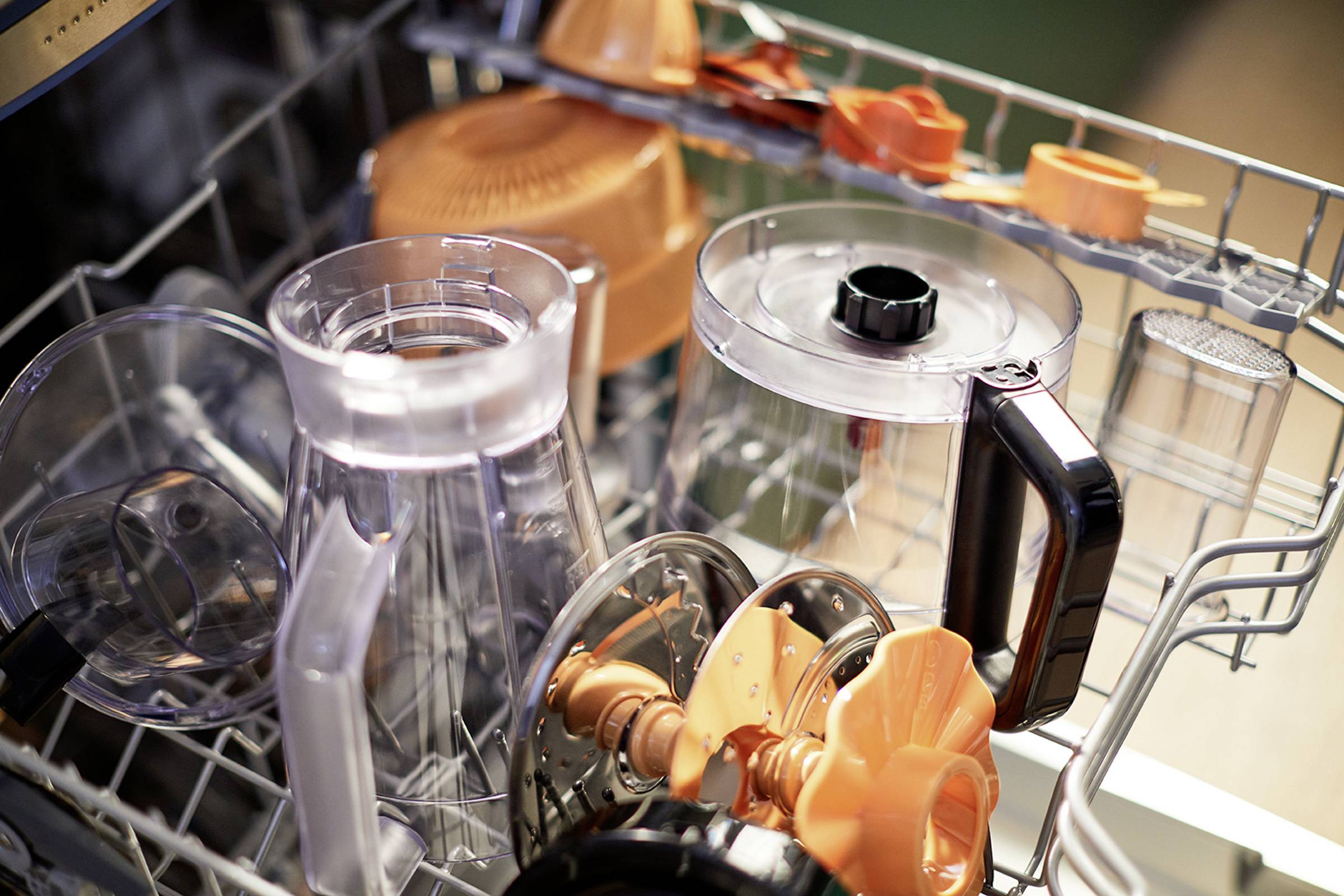 Vaatwasser met diverse vaatwasonderdelen, waaronder transparante en oranje containers en opzetstukken.