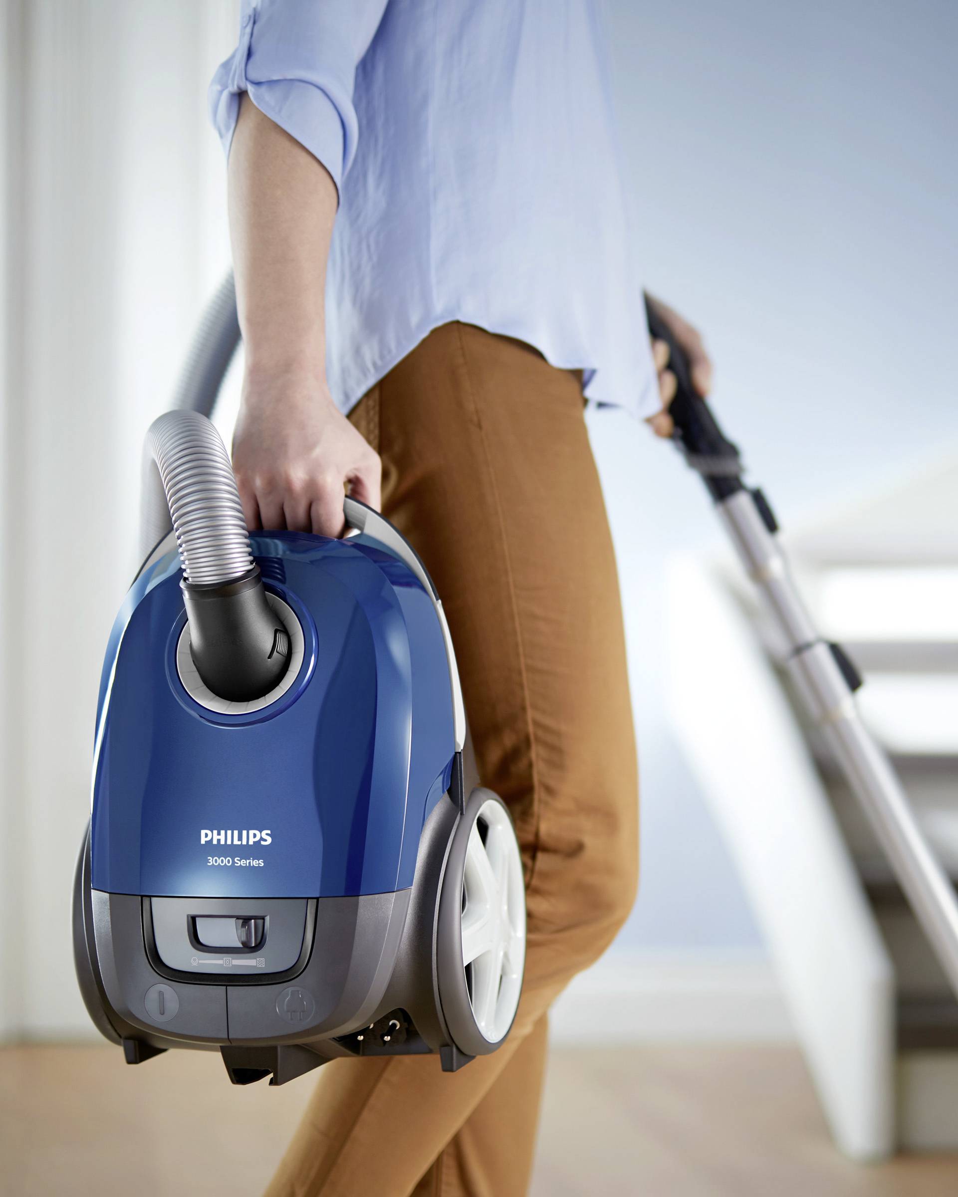 Een persoon draagt een blauwe stofzuiger van het merk Philips 3000 Series terwijl hij een trap oploopt.