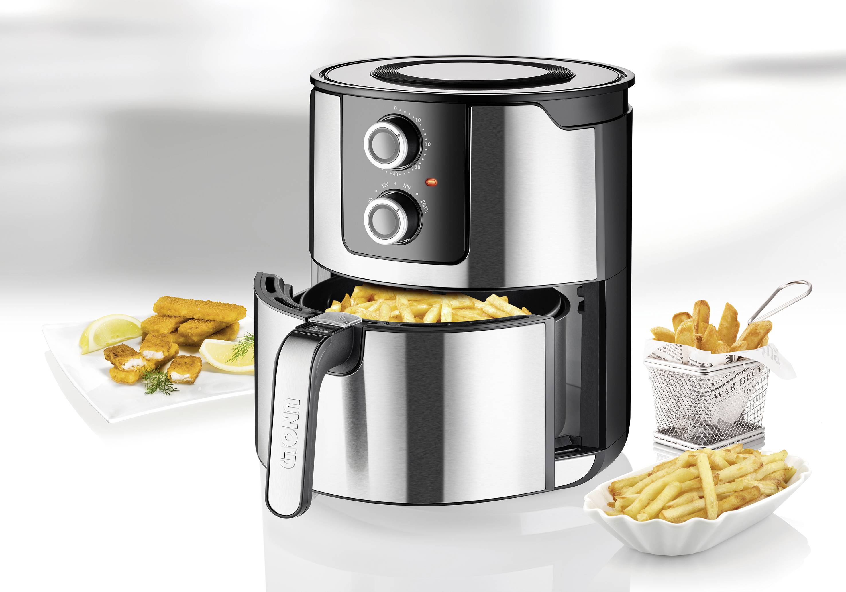 Zilveren airfryer met open lade gevuld met frietjes. Naast een bord met knapperige hapjes en citroenwedges.