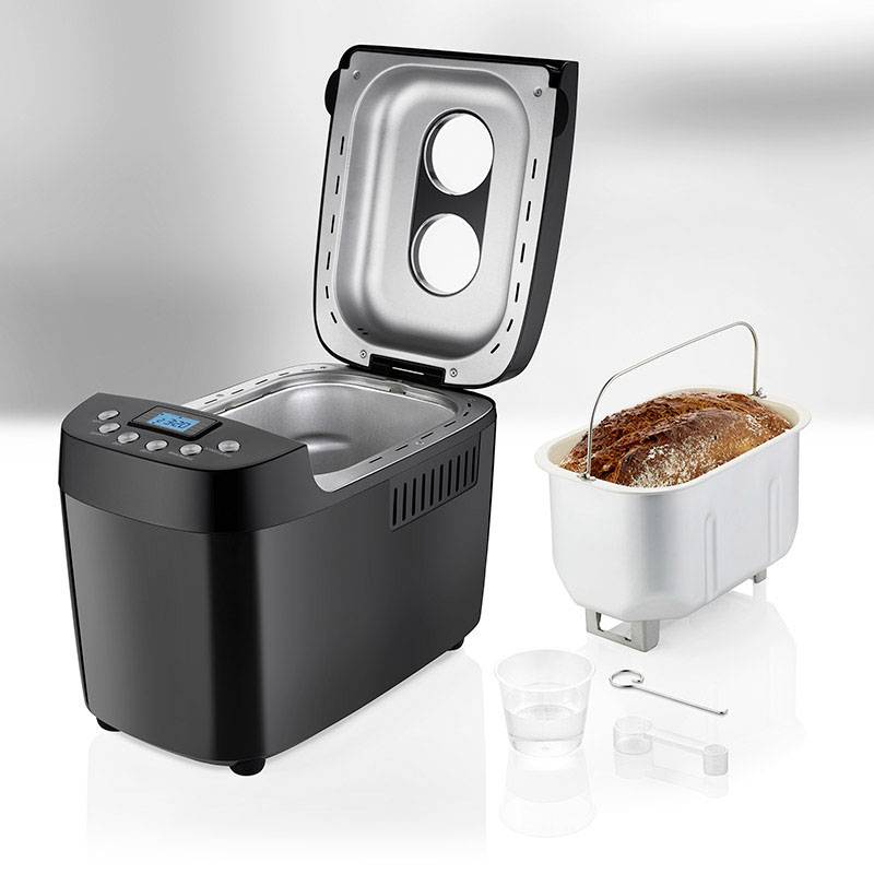 Broodbakmachine met open deksel, broodvorm met gebakken brood, naast een maatbeker, deeghaak en maatlepel.